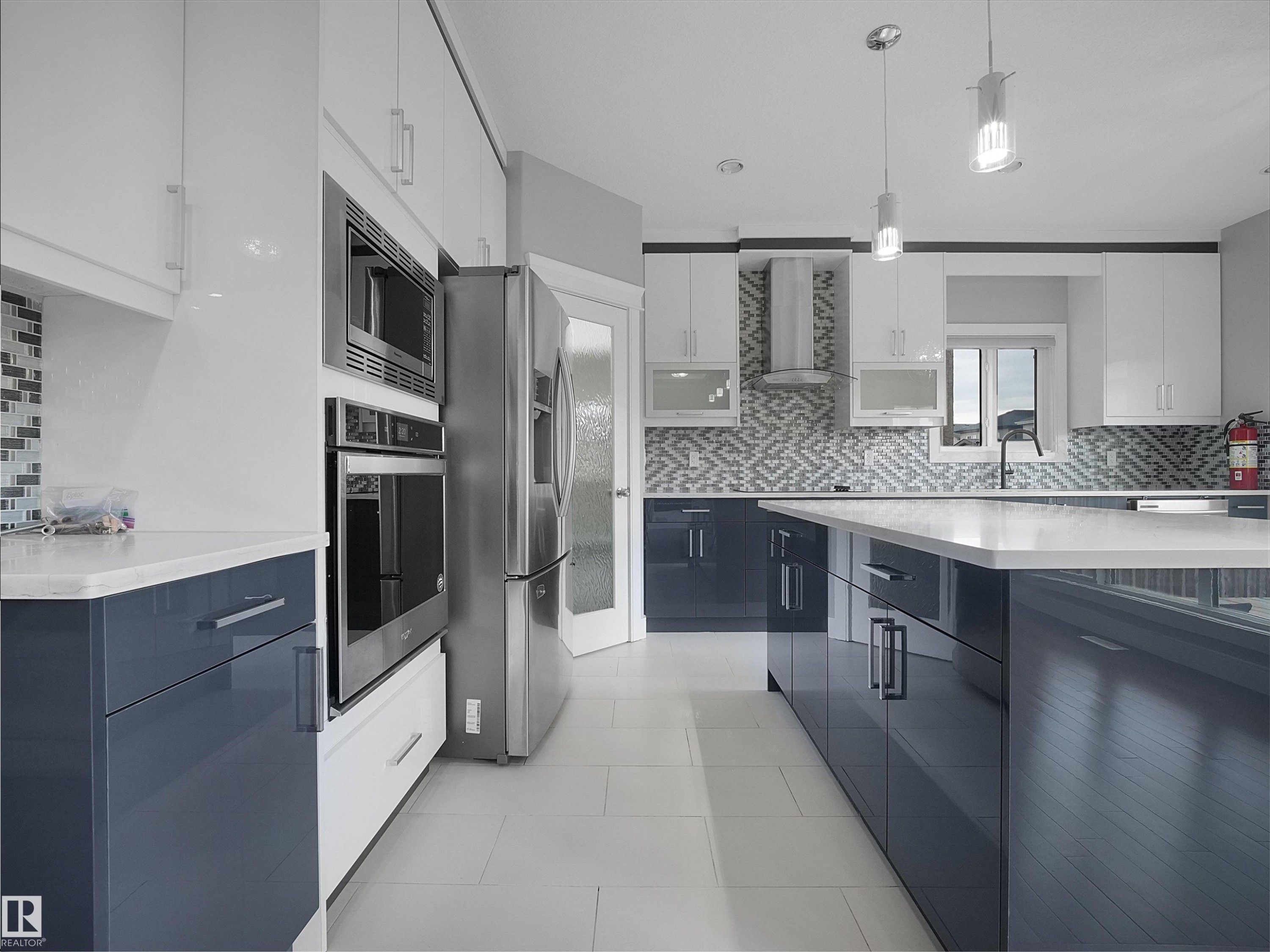 Modern kitchen featuring two-tone cabinetry, stainless steel appliances, a large island with a solid surface countertop, and a mosaic tile backsplash - 17020 62 Street Nw, Edmonton, AB - Indoor Photo Showing Kitchen With Upgraded Kitchen