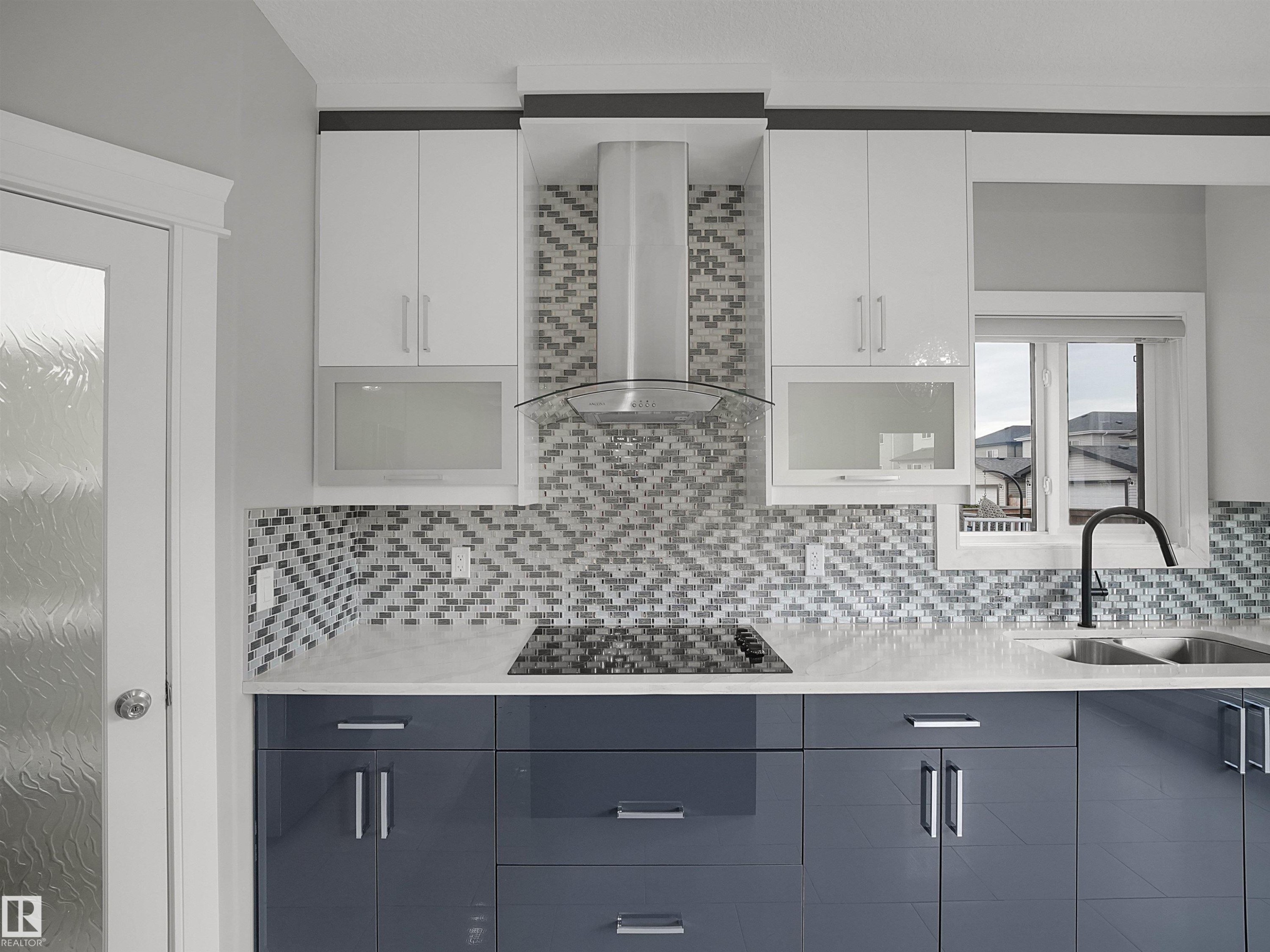 Two-tone cabinetry with white upper and grey lower units, mosaic tile backsplash, built-in cooktop, stainless steel range hood, and double basin sink with a black gooseneck faucet - 17020 62 Street Nw, Edmonton, AB - Indoor Photo Showing Kitchen With Double Sink With Upgraded Kitchen