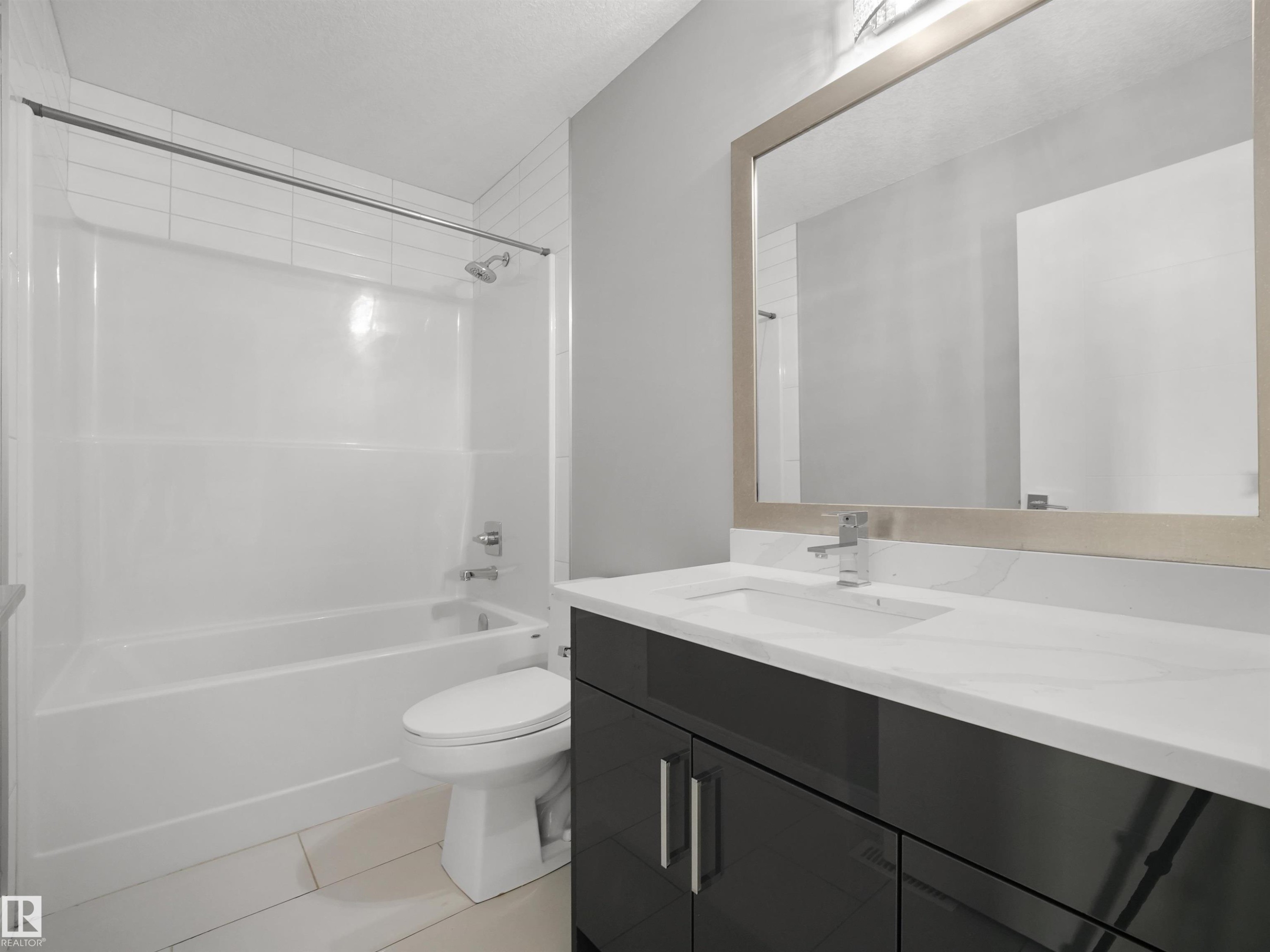 Bathroom featuring a white bathtub, ceramic wall tiles, contemporary vanity with a white countertop and integrated sink, and a framed mirror - 17020 62 Street Nw, Edmonton, AB - Indoor Photo Showing Bathroom