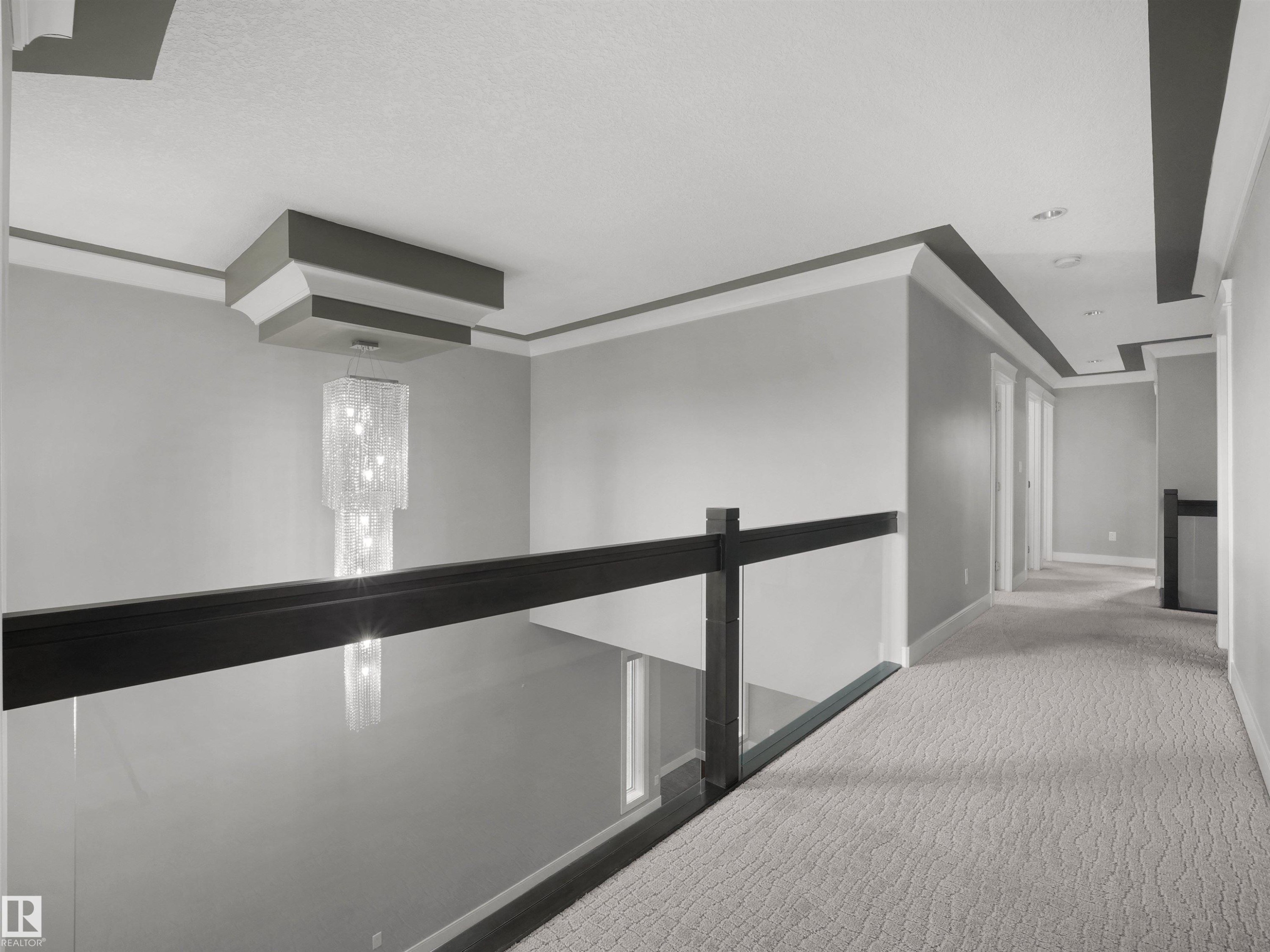 Open landing with a glass panel railing, dark wood-tone handrail, and patterned carpeting - 17020 62 Street Nw, Edmonton, AB - Indoor Photo Showing Other Room