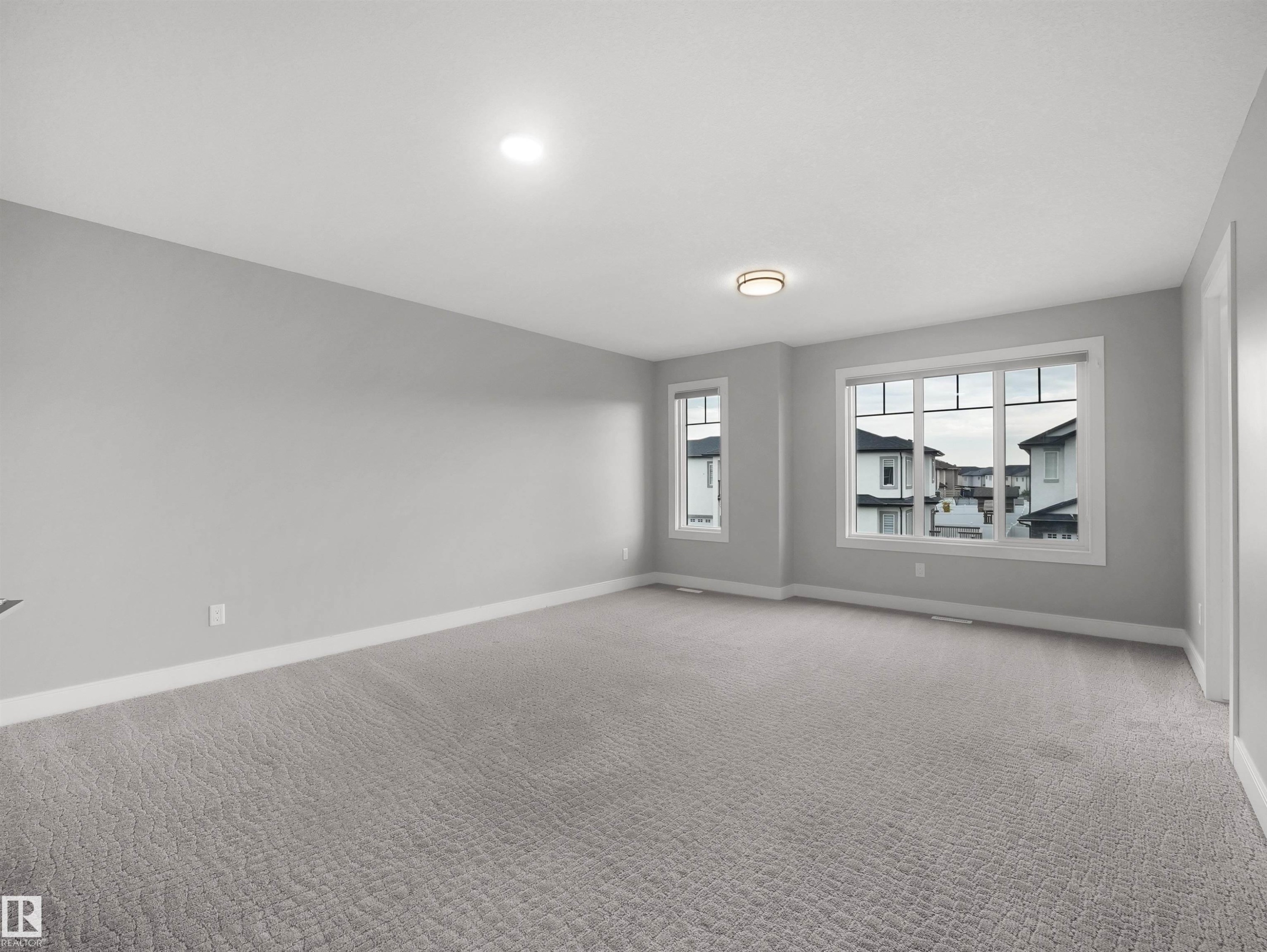 Spacious room with light gray walls, textured gray carpeting, multiple windows, and recessed lighting - 17020 62 Street Nw, Edmonton, AB - Indoor