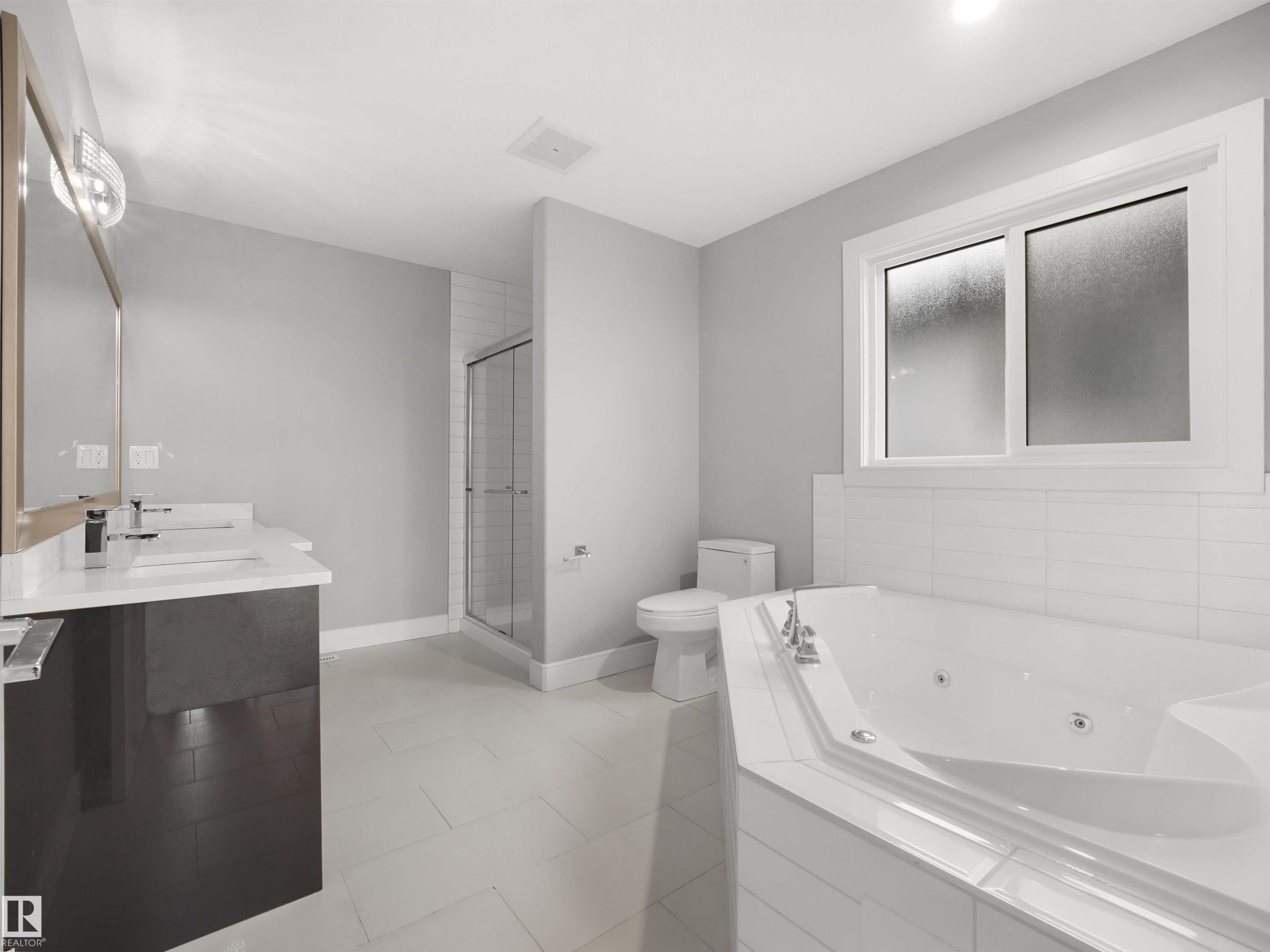 Dual vanity with undermount sinks, corner jetted tub, separate glass-enclosed shower, and large frosted window - 17020 62 Street Nw, Edmonton, AB - Indoor Photo Showing Bathroom