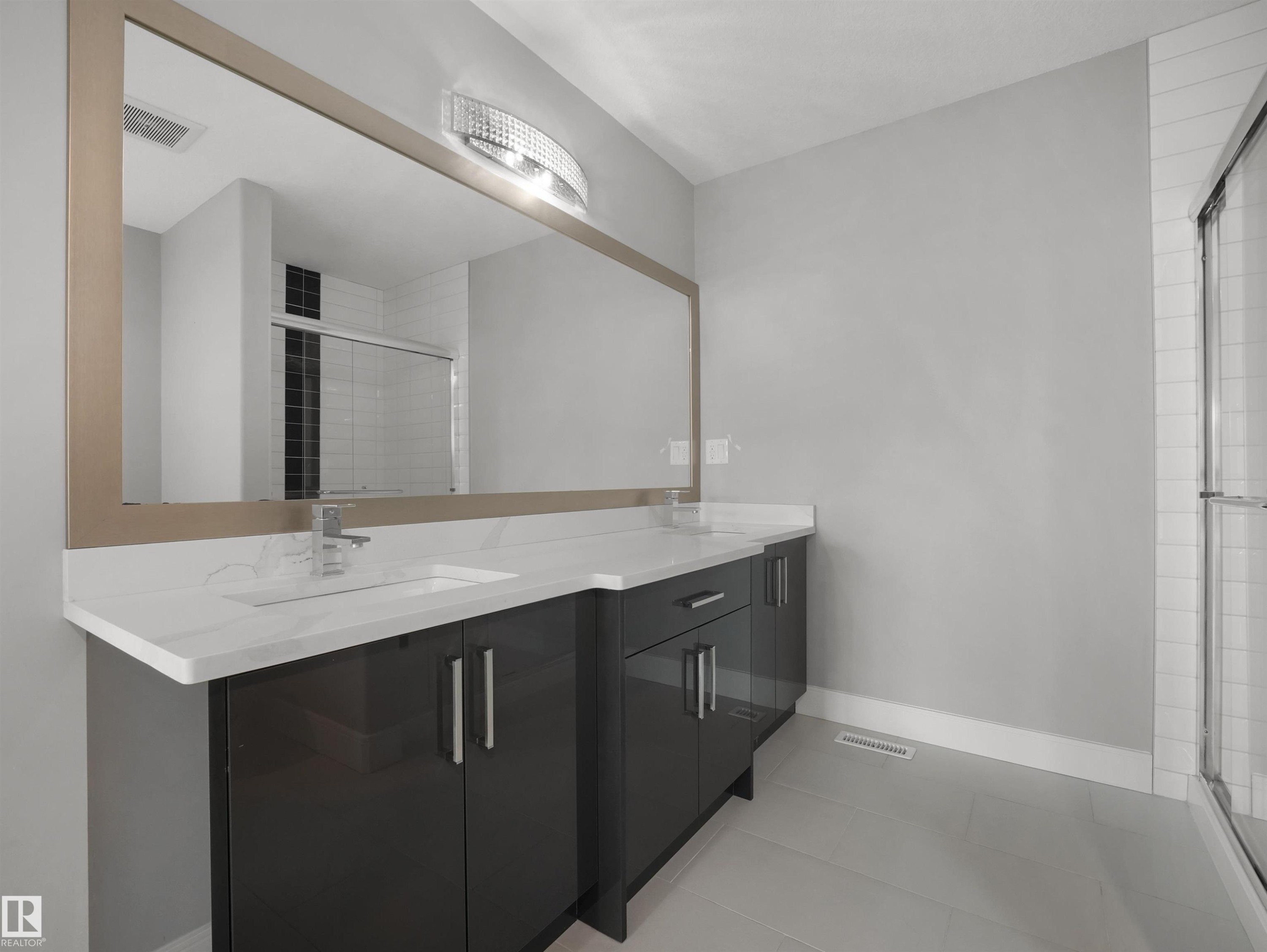 Dual vanity with white countertops, chrome fixtures, a broad framed mirror, and an illuminated light fixture - 17020 62 Street Nw, Edmonton, AB - Indoor Photo Showing Bathroom
