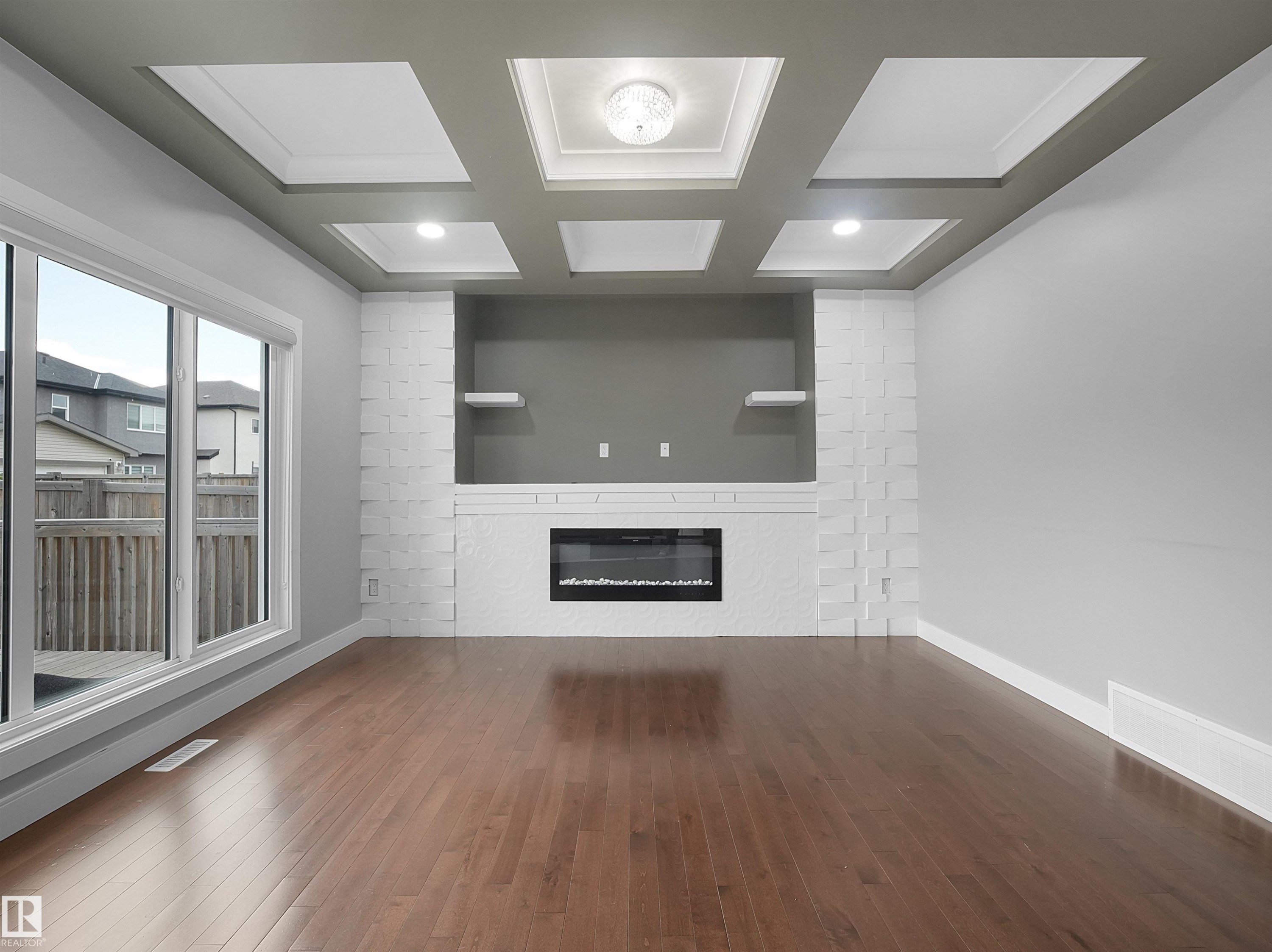 Wood-finish flooring, white brick fireplace surround, built-in electric fireplace, integrated shelving, coffered ceiling with recessed lighting - 17020 62 Street Nw, Edmonton, AB - Indoor Photo Showing Other Room With Fireplace