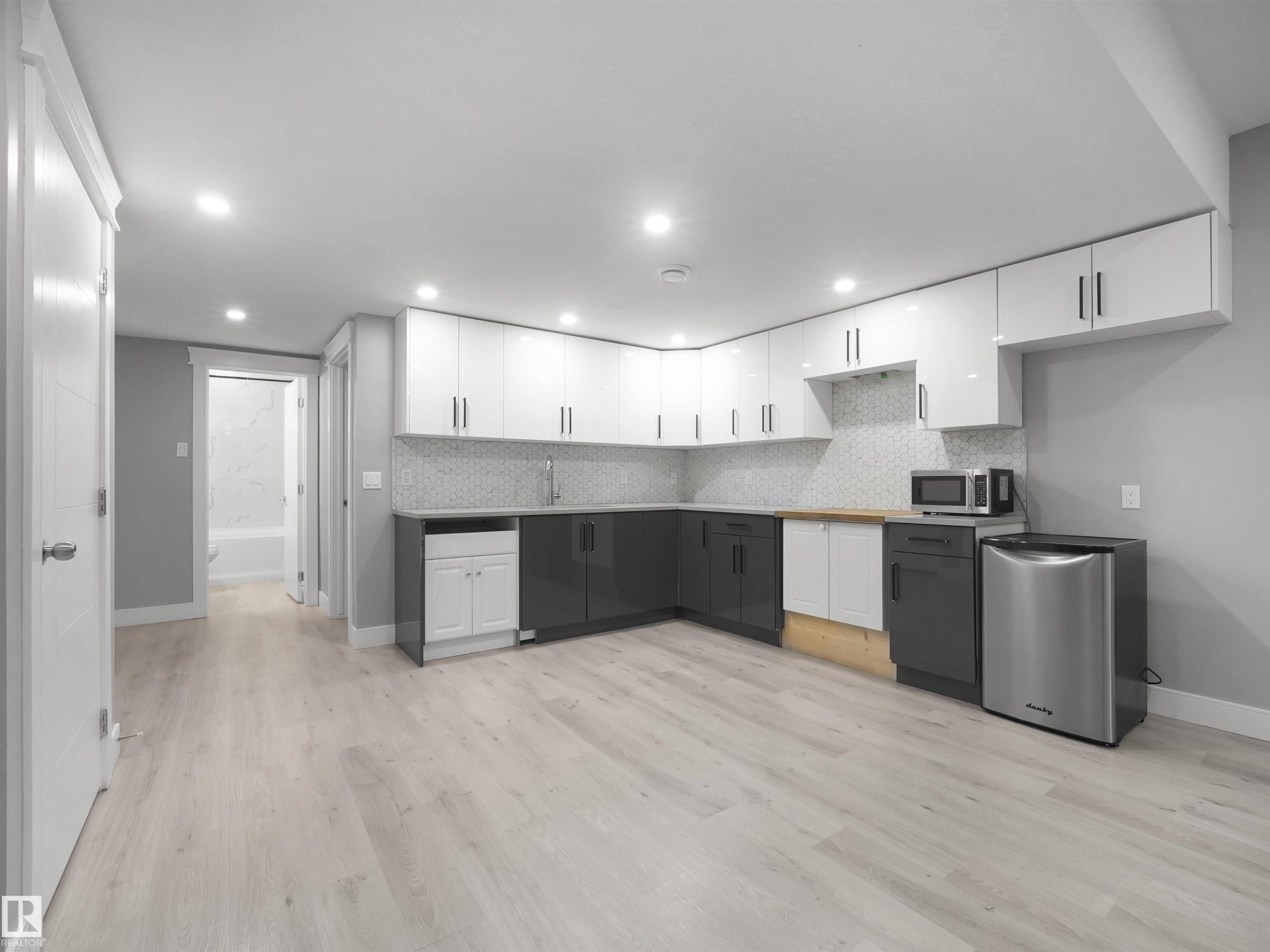 Corner kitchen with two-tone cabinetry, mosaic tile backsplash, and light wood-finish flooring - 17020 62 Street Nw, Edmonton, AB - Indoor Photo Showing Kitchen