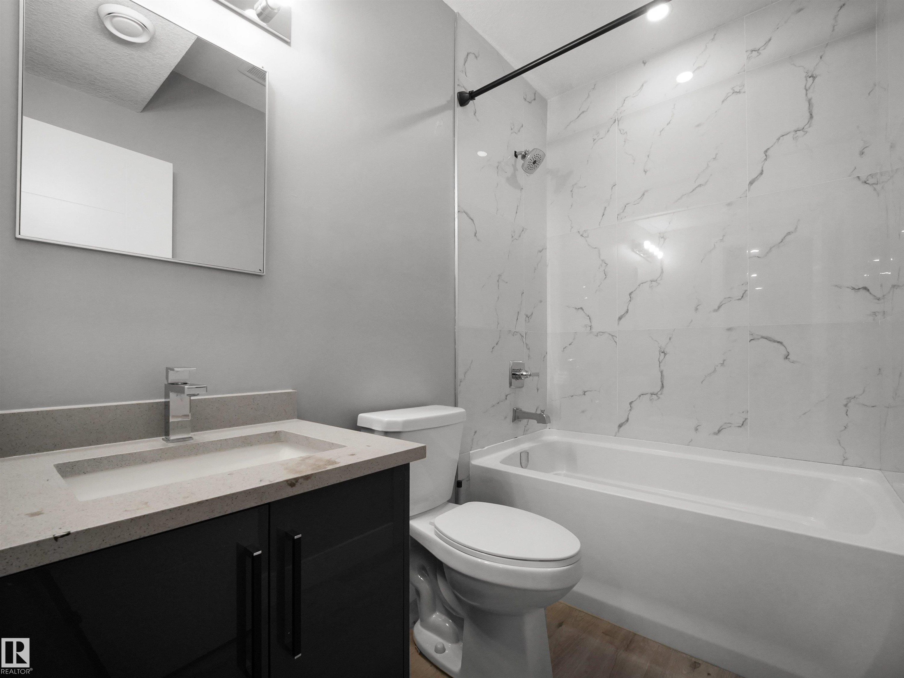Bathroom featuring a dark wood-finish vanity with a light countertop, a rectangular sink with a chrome faucet, a white toilet, and a white tiled shower with a black shower rod - 17020 62 Street Nw, Edmonton, AB - Indoor Photo Showing Bathroom