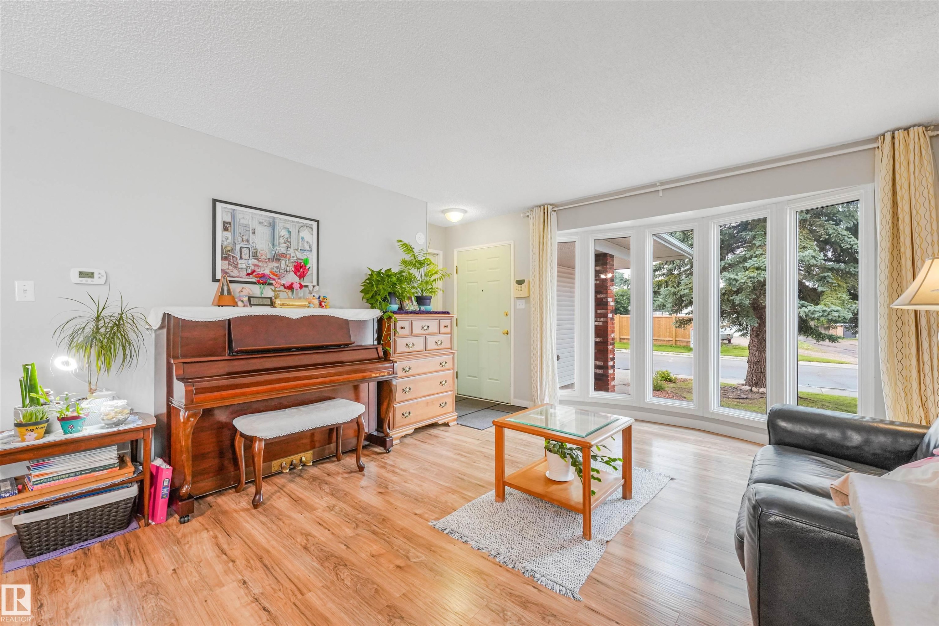 Bright living space featuring a bay window with multiple panes, wood-finish flooring, light gray wall tones, and a light-colored entry door - 18611 57 Avenue Nw, Edmonton, AB - Indoor Photo Showing Living Room