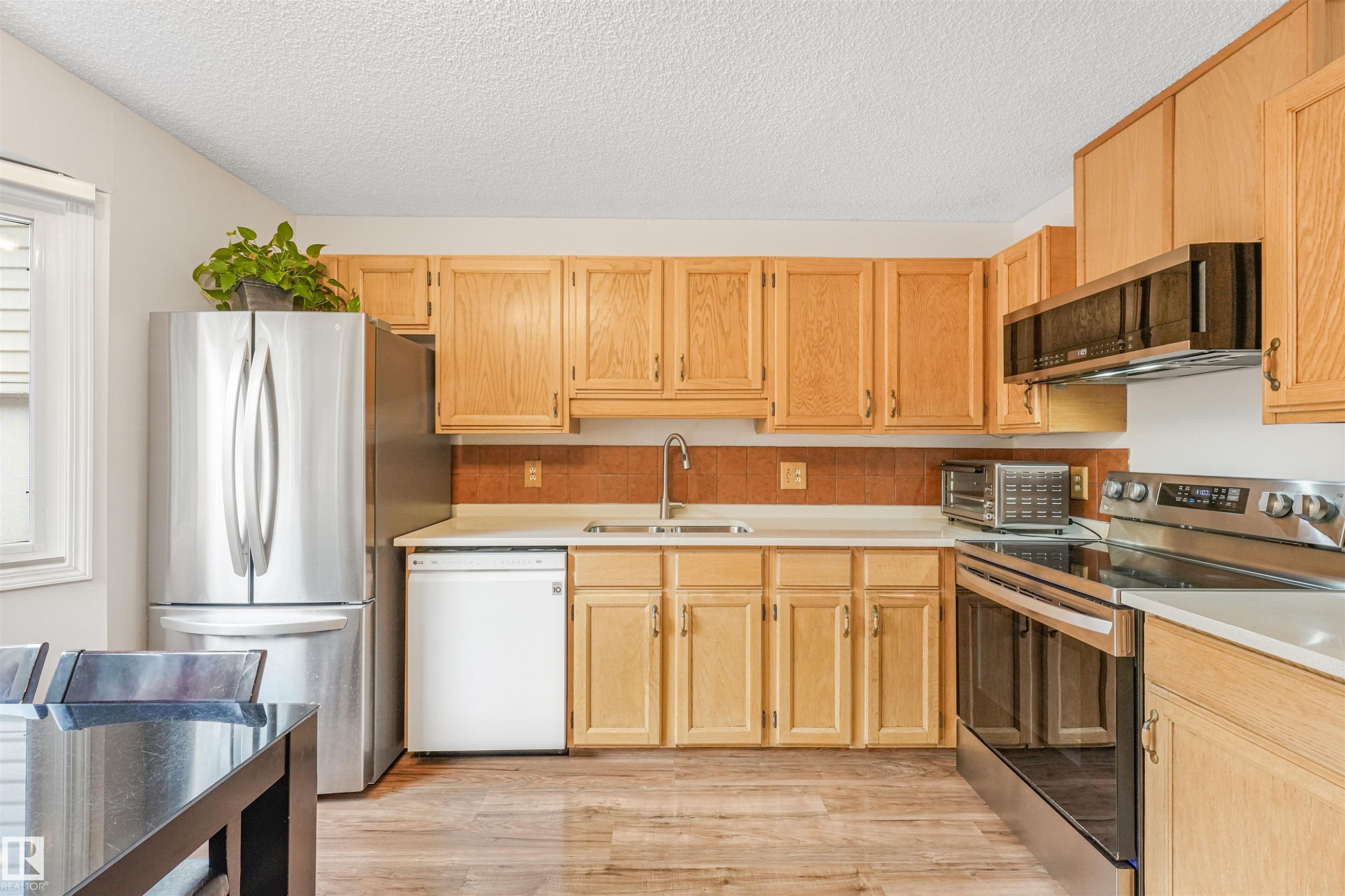 Kitchen featuring natural wood cabinetry, stainless steel appliances, light-toned countertops, and wood-finish flooring - 18611 57 Avenue Nw, Edmonton, AB - Indoor Photo Showing Kitchen
