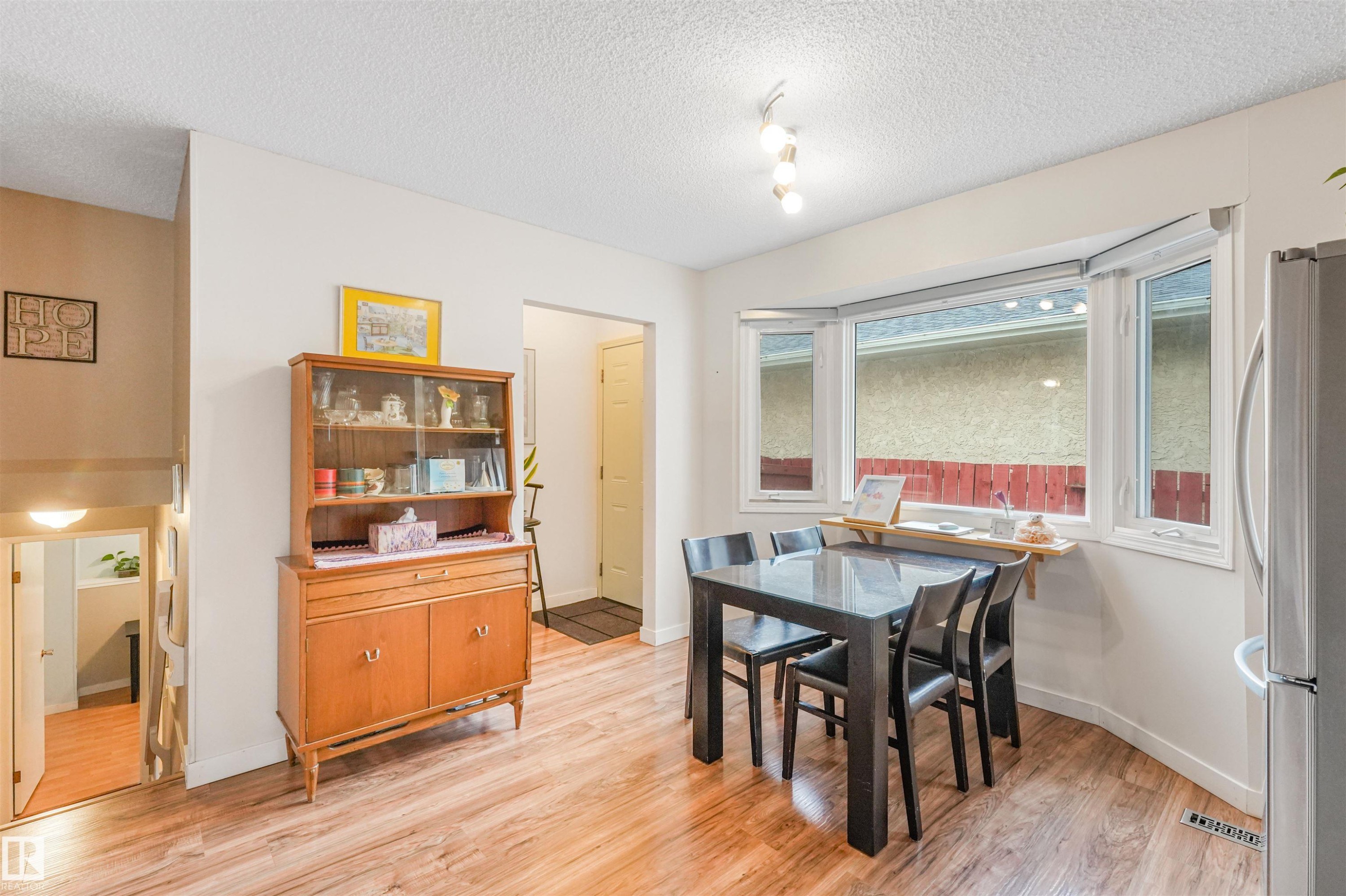 Open-concept dining area featuring wood-finish flooring, a contemporary ceiling light fixture, and a large bay window - 18611 57 Avenue Nw, Edmonton, AB - Indoor Photo Showing Dining Room