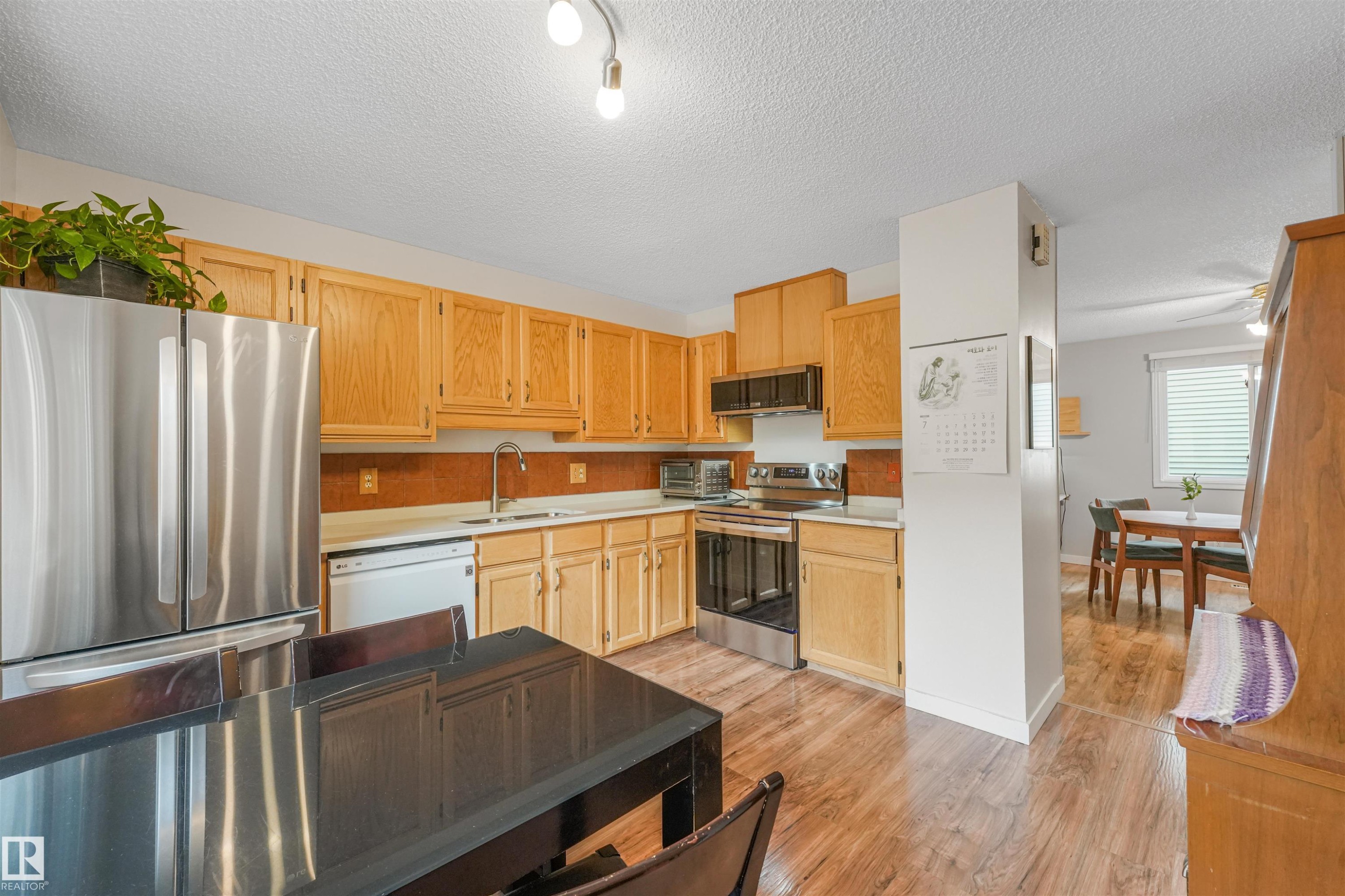 Bright kitchen featuring wood-finish flooring, light wood cabinetry, and stainless steel appliances - 18611 57 Avenue Nw, Edmonton, AB - Indoor Photo Showing Kitchen