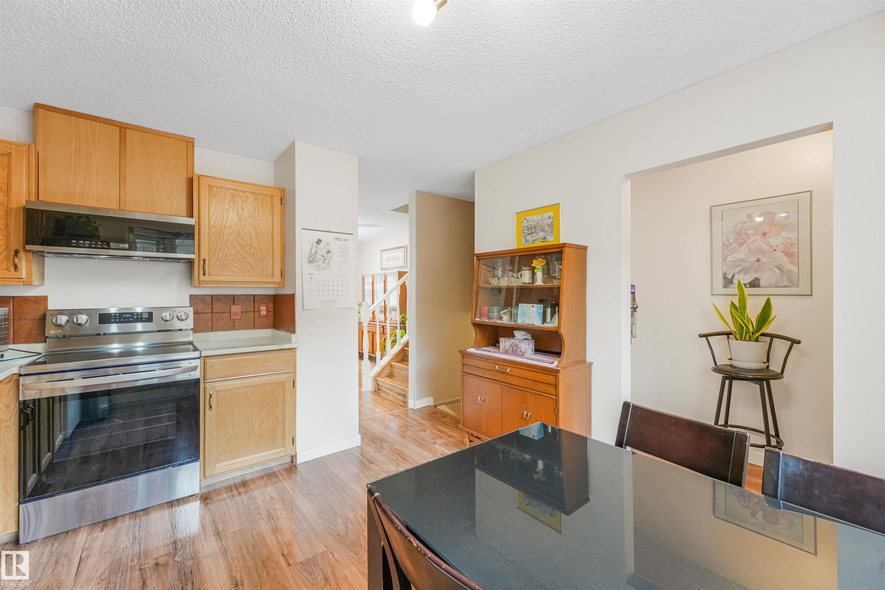 Kitchen featuring wood-finish flooring, light wood cabinetry, stainless steel range with overhead microwave, and tile backsplash - 18611 57 Avenue Nw, Edmonton, AB - Indoor Photo Showing Kitchen