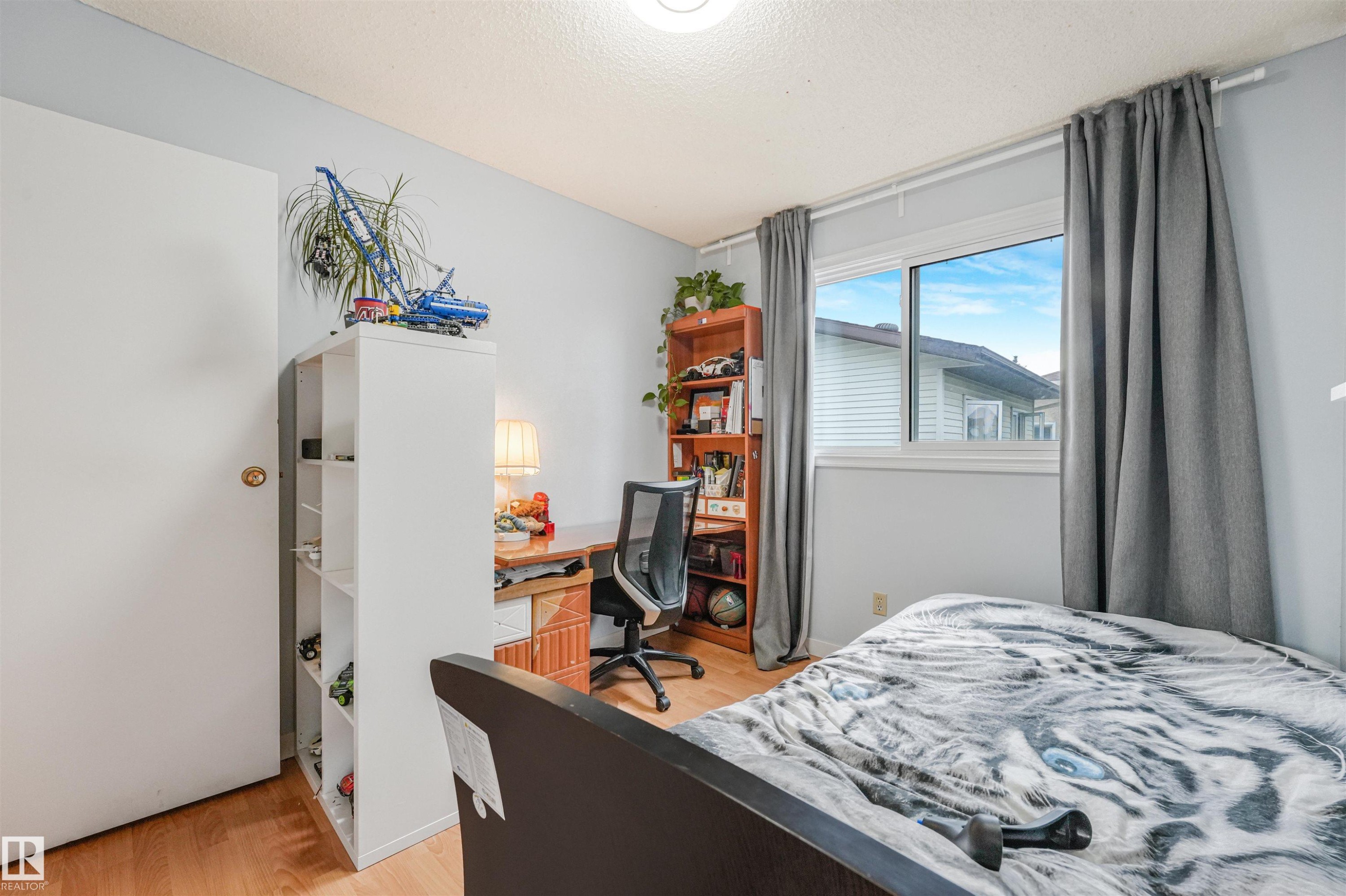 Room featuring wood-finish flooring, a double-pane window with a light blue exterior, and a built-in closet with a white door - 18611 57 Avenue Nw, Edmonton, AB - Indoor Photo Showing Bedroom