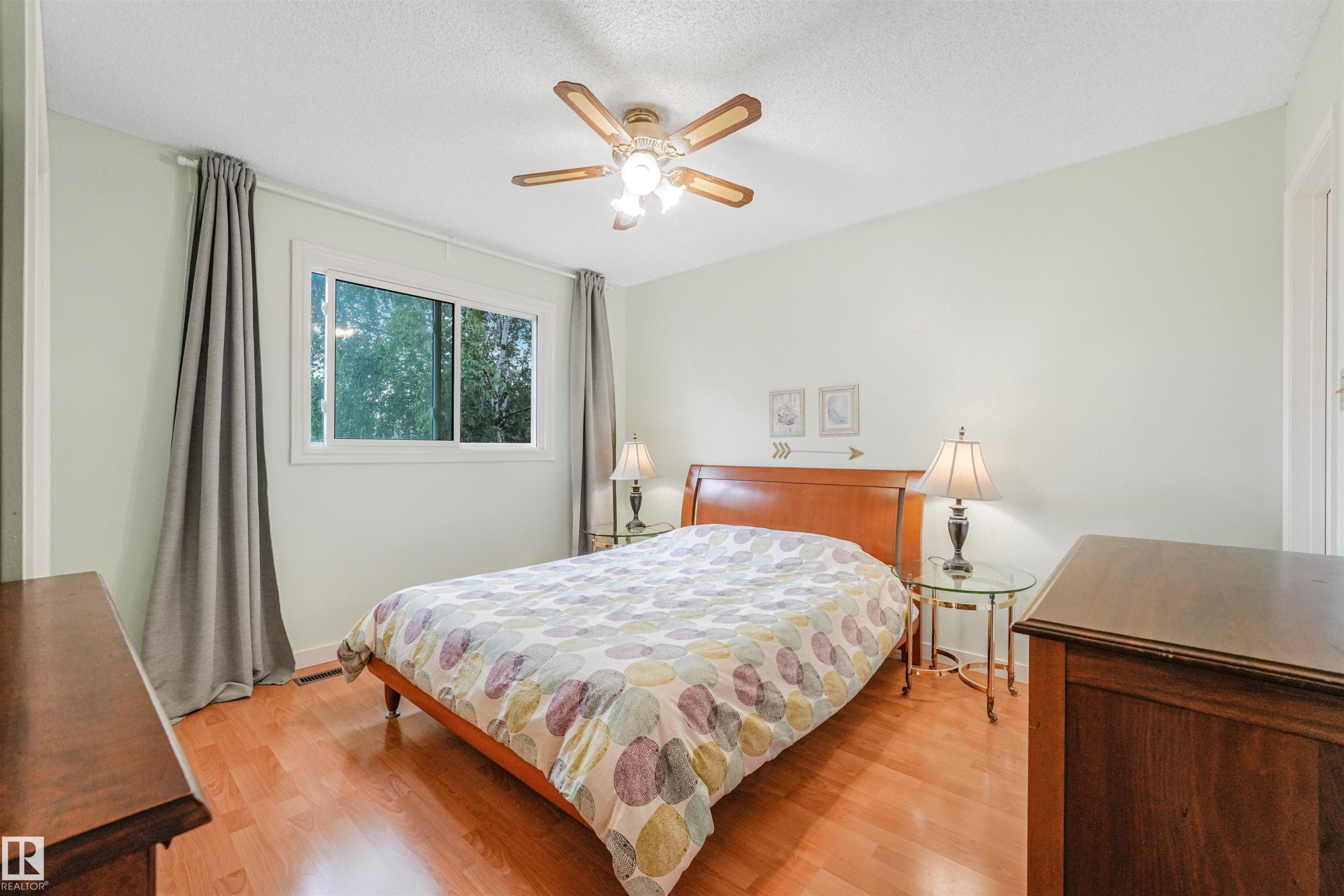 Bright room featuring wood-finish flooring, a ceiling fan with integrated lighting, and a window with white trim - 18611 57 Avenue Nw, Edmonton, AB - Indoor Photo Showing Bedroom