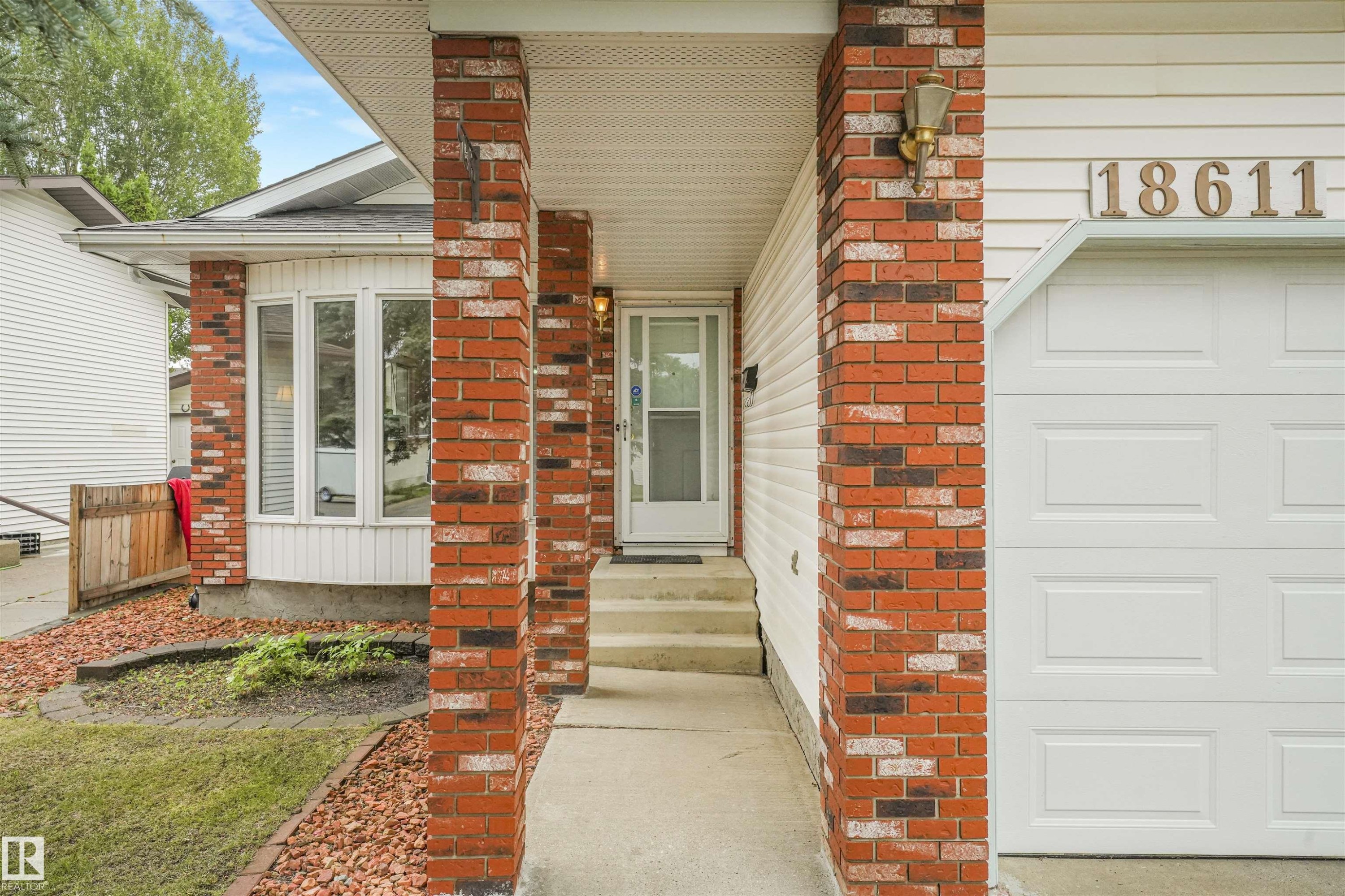 Exterior featuring brick columns, bay windows, white siding, and a white garage door - 18611 57 Avenue Nw, Edmonton, AB - Outdoor