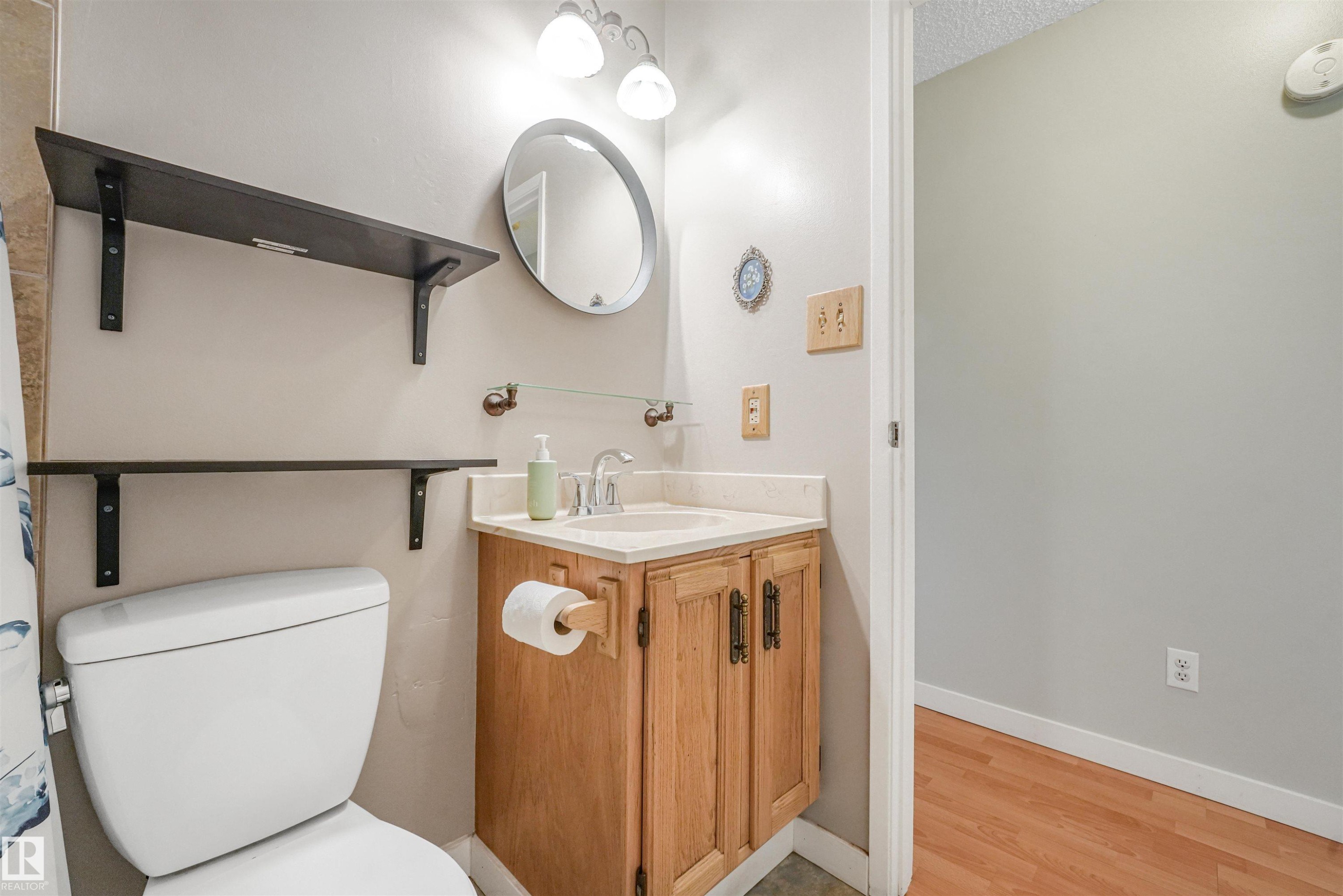 Bathroom featuring a vanity with a light wood-finish cabinet and countertop, a round wall-mounted mirror, and overhead vanity lighting - 18611 57 Avenue Nw, Edmonton, AB - Indoor