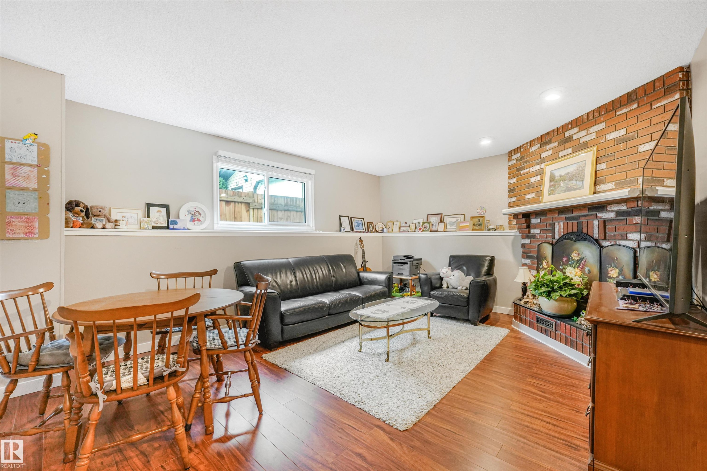 Spacious living area featuring wood-finish flooring, a brick fireplace with a white mantel, and recessed lighting - 18611 57 Avenue Nw, Edmonton, AB - Indoor