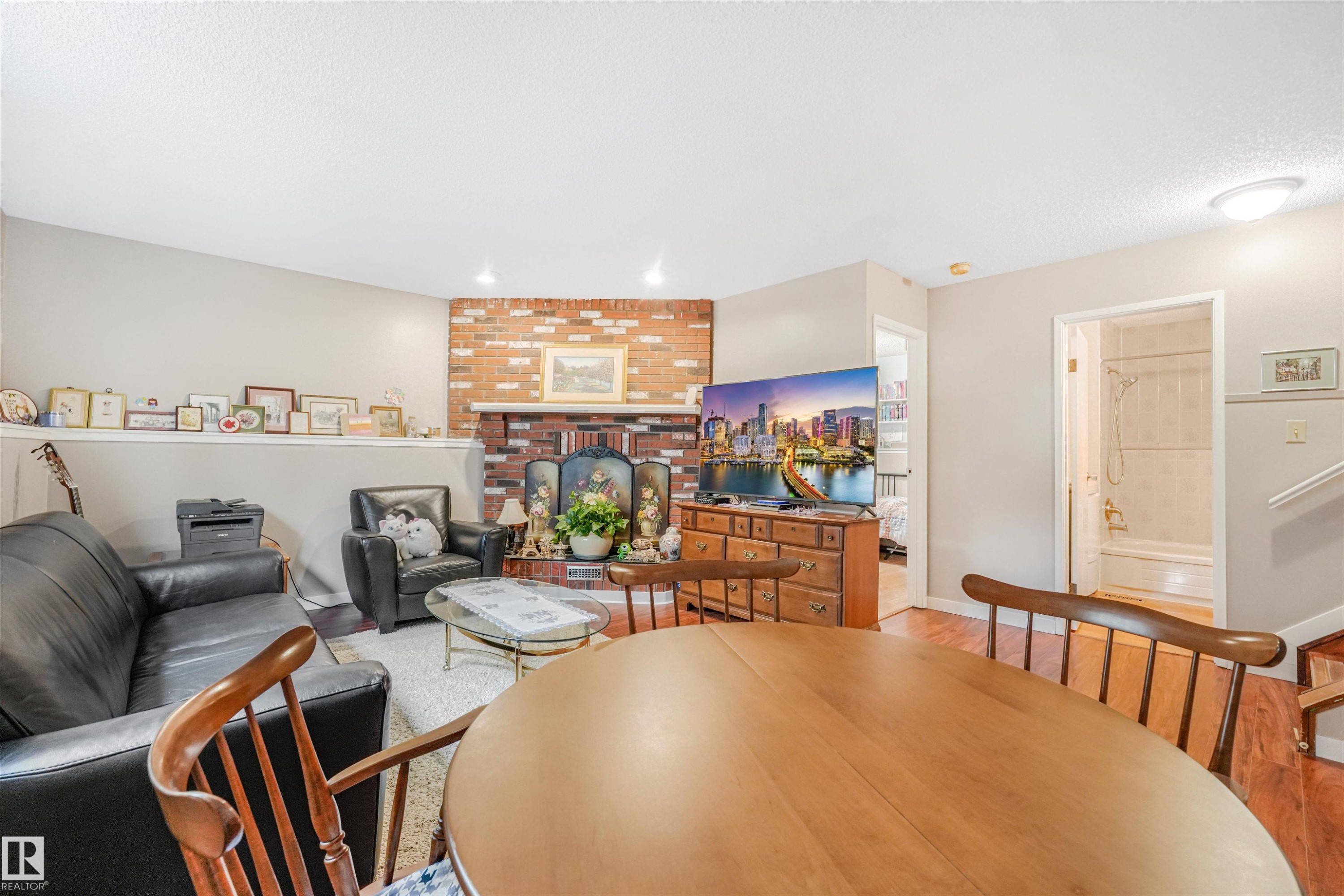 Living area featuring a brick fireplace with a wood mantel, overhead recessed lighting, and wood-finish flooring - 18611 57 Avenue Nw, Edmonton, AB - Indoor