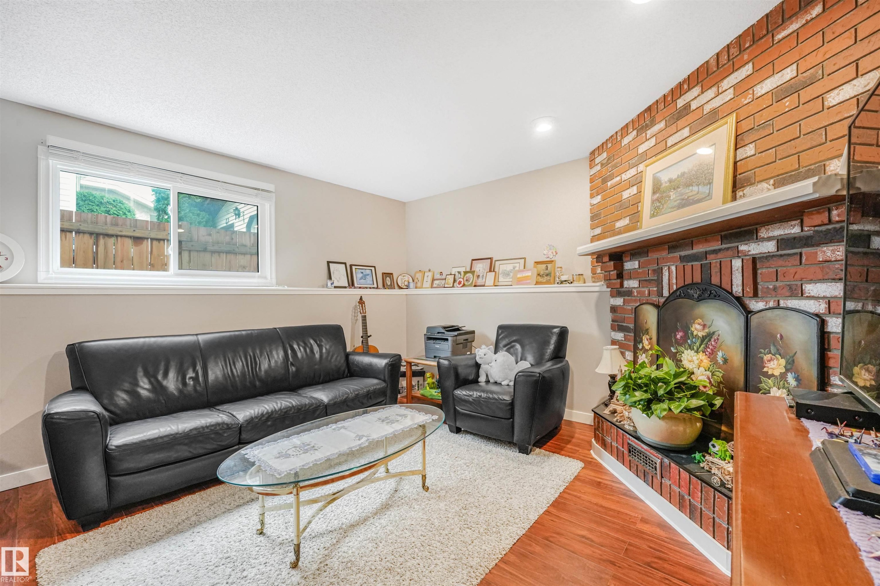 Brick fireplace with a white mantel, wood-finish flooring, recessed lighting, and a window with white trim - 18611 57 Avenue Nw, Edmonton, AB - Indoor Photo Showing Living Room With Fireplace