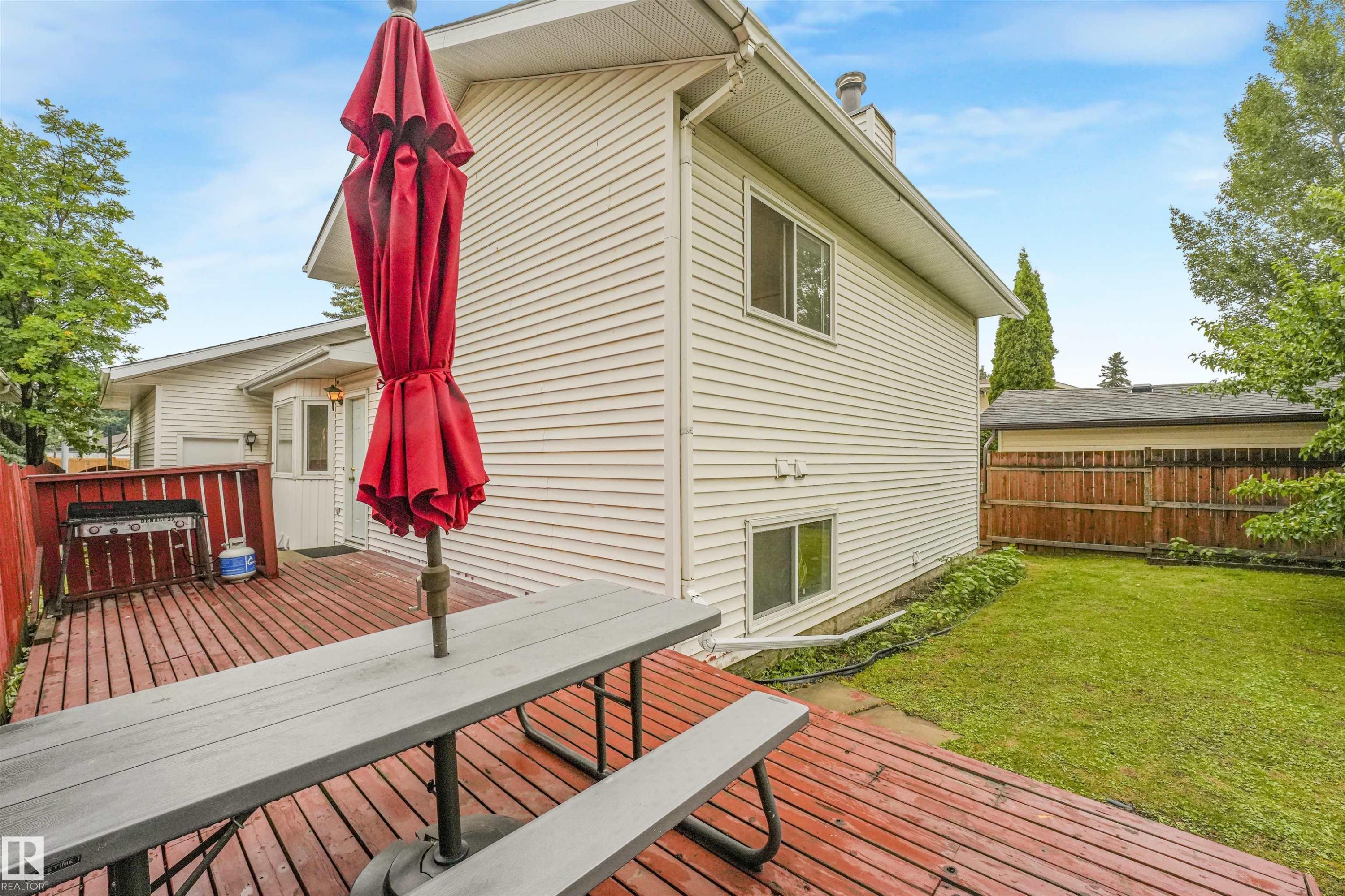 Spacious backyard featuring a multi-level wood deck, manicured lawn, wood privacy fence, and white vinyl siding - 18611 57 Avenue Nw, Edmonton, AB - Outdoor With Deck Patio Veranda With Exterior