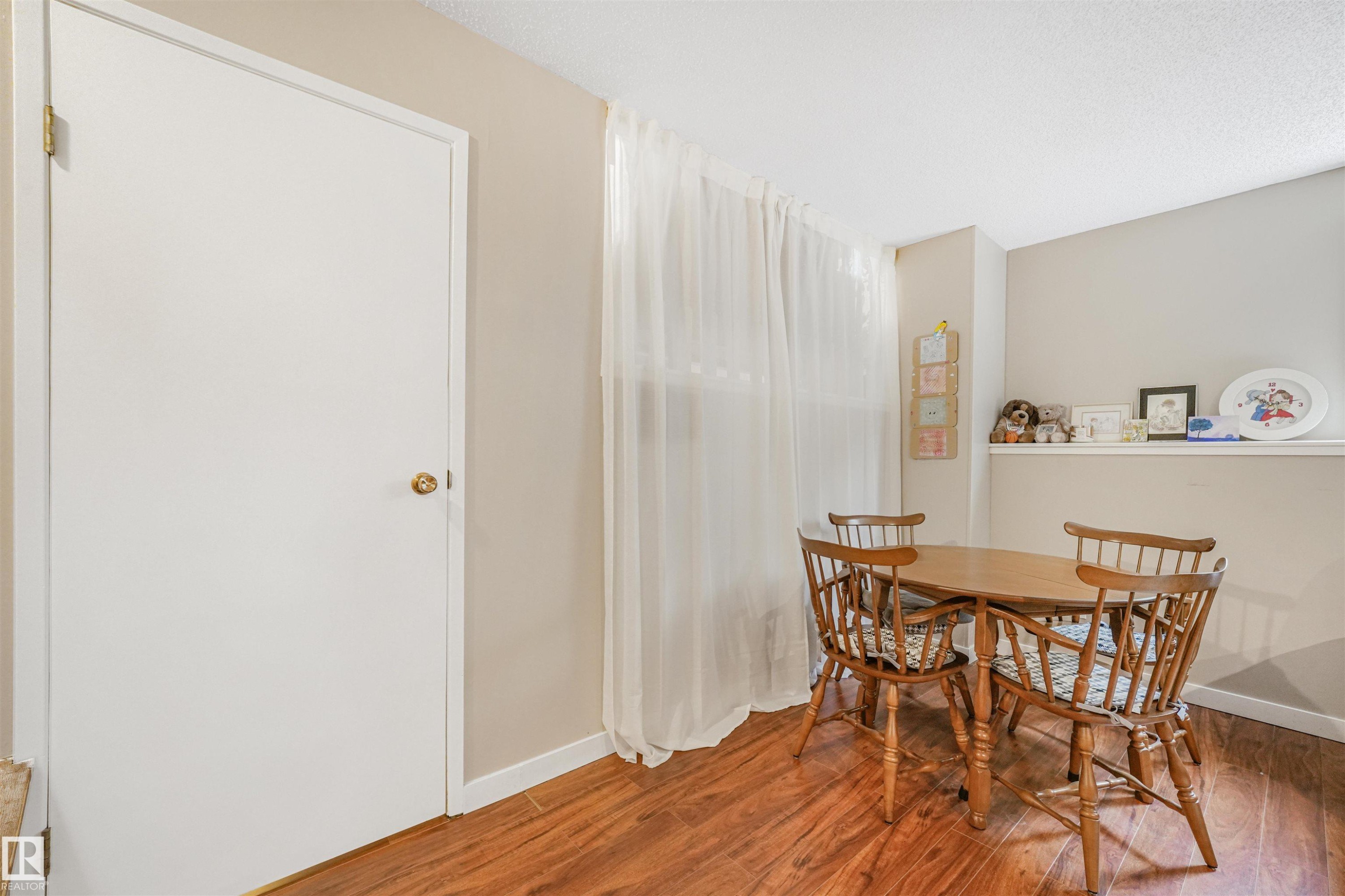 Dining area featuring wood-finish flooring, a window with sheer white curtains, and a built-in wall shelf - 18611 57 Avenue Nw, Edmonton, AB - Indoor Photo Showing Dining Room