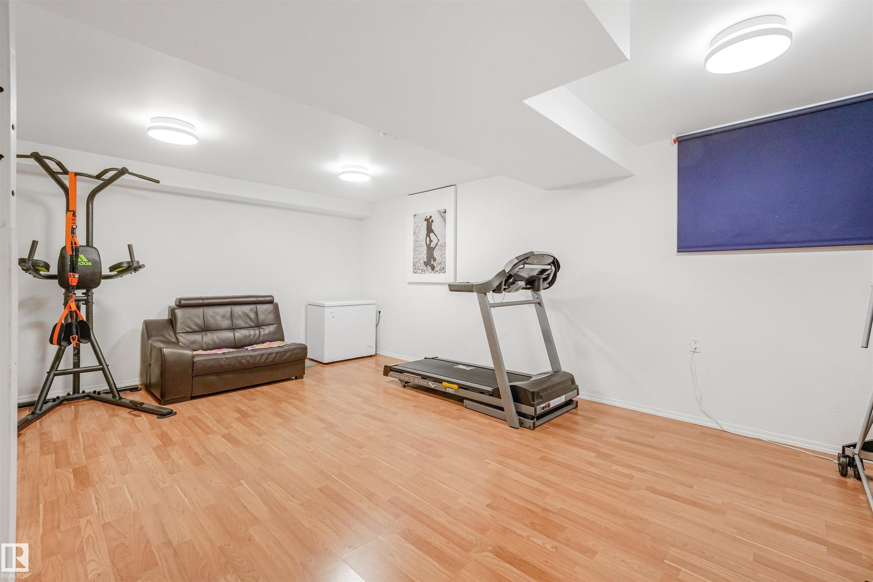 Open concept room featuring wood-finish flooring, white walls, and contemporary flush-mount lighting fixtures - 18611 57 Avenue Nw, Edmonton, AB - Indoor Photo Showing Gym Room