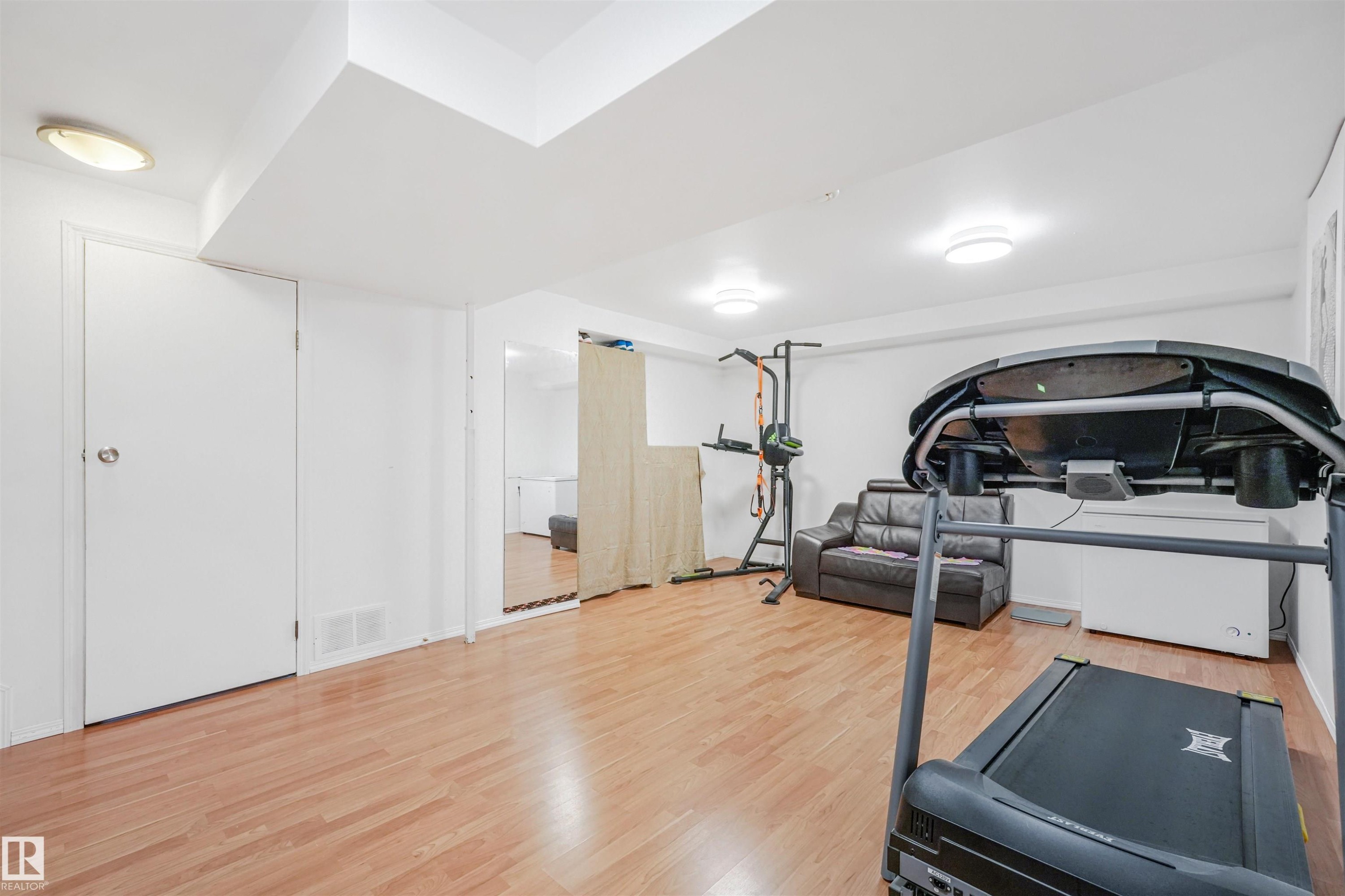 Finished lower level with wood-finish flooring, recessed lighting, white walls, and a white door with silver hardware - 18611 57 Avenue Nw, Edmonton, AB - Indoor Photo Showing Gym Room