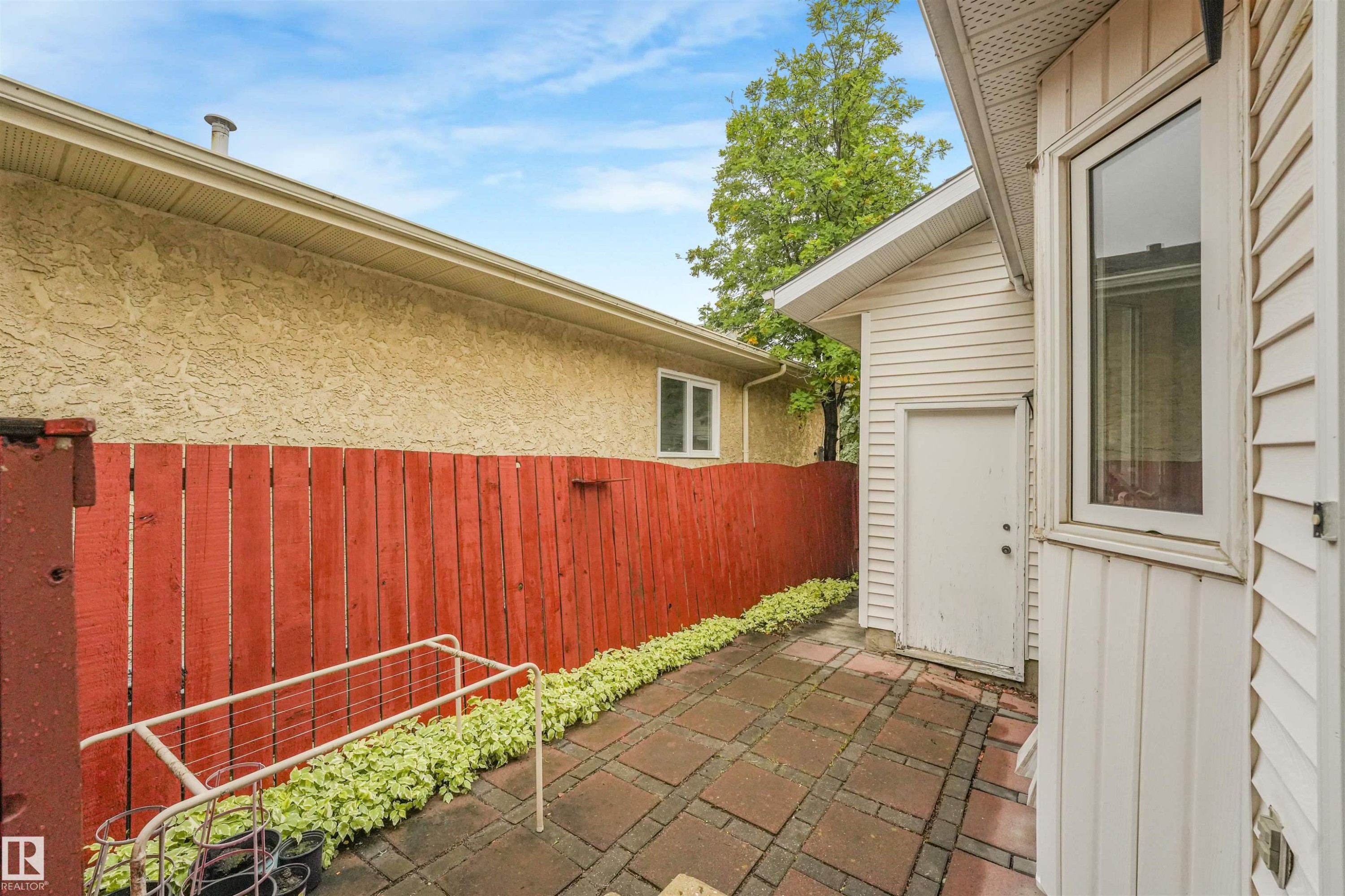 Private outdoor patio featuring brick paver flooring, a red wood privacy fence, and integrated landscaping - 18611 57 Avenue Nw, Edmonton, AB - Outdoor With Exterior
