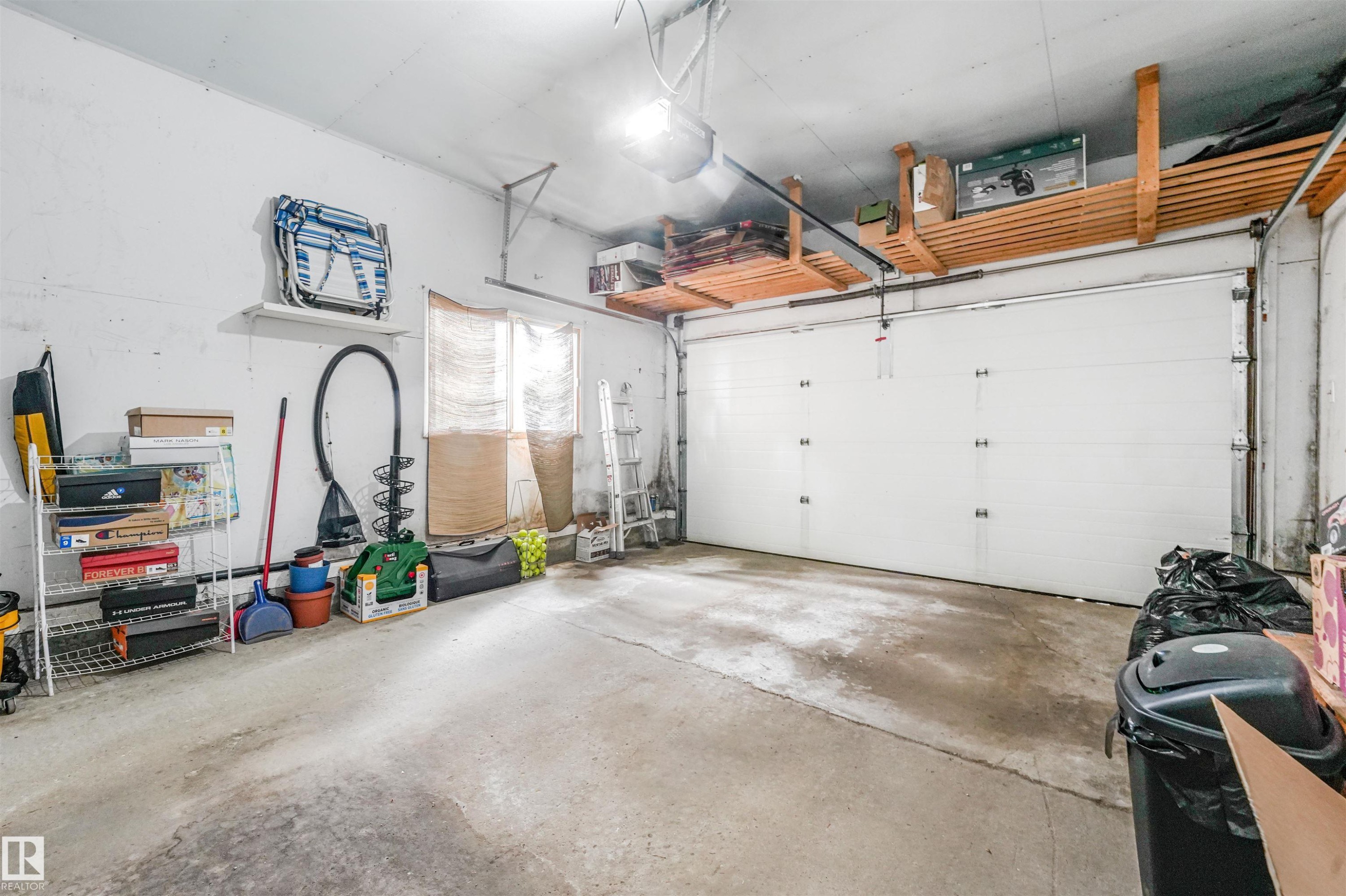 Single-car garage featuring a white overhead door, concrete flooring, and overhead wood slat storage shelving - 18611 57 Avenue Nw, Edmonton, AB - Indoor Photo Showing Garage