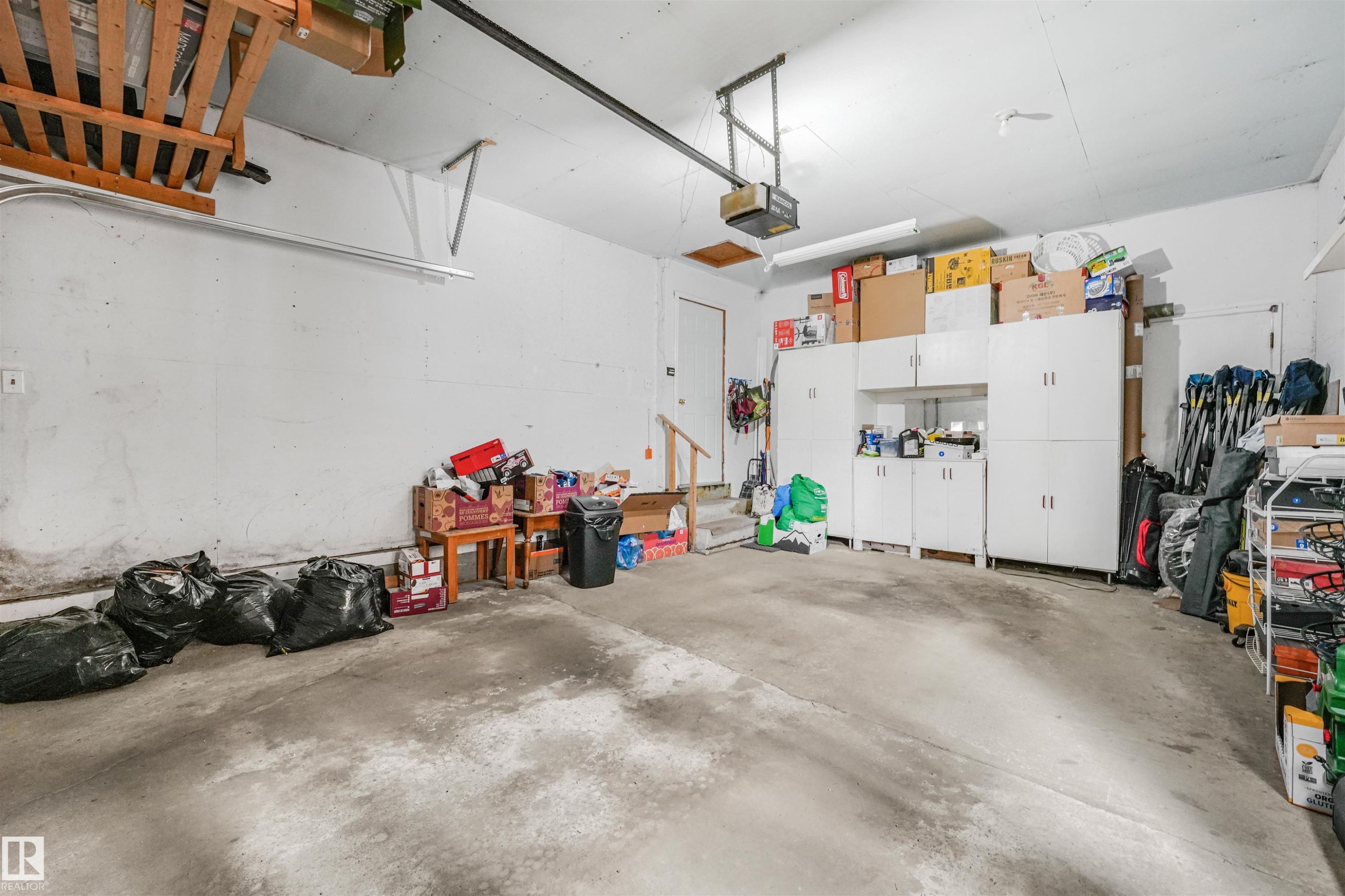 Spacious garage featuring concrete flooring, built-in white cabinetry, overhead storage, and a garage door opener - 18611 57 Avenue Nw, Edmonton, AB - Indoor Photo Showing Garage