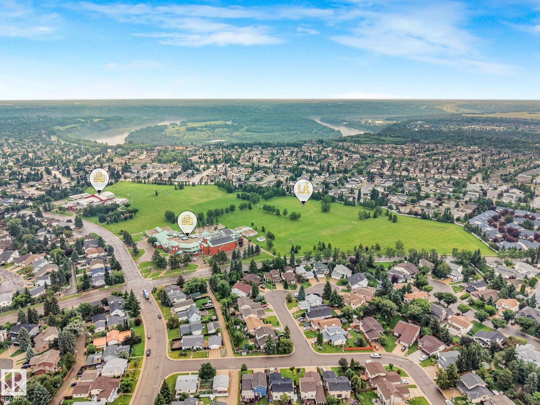 Aerial perspective showcasing a residential neighborhood with verdant green spaces, a winding river in the distance, and established community buildings - 18611 57 Avenue Nw, Edmonton, AB - Outdoor With View