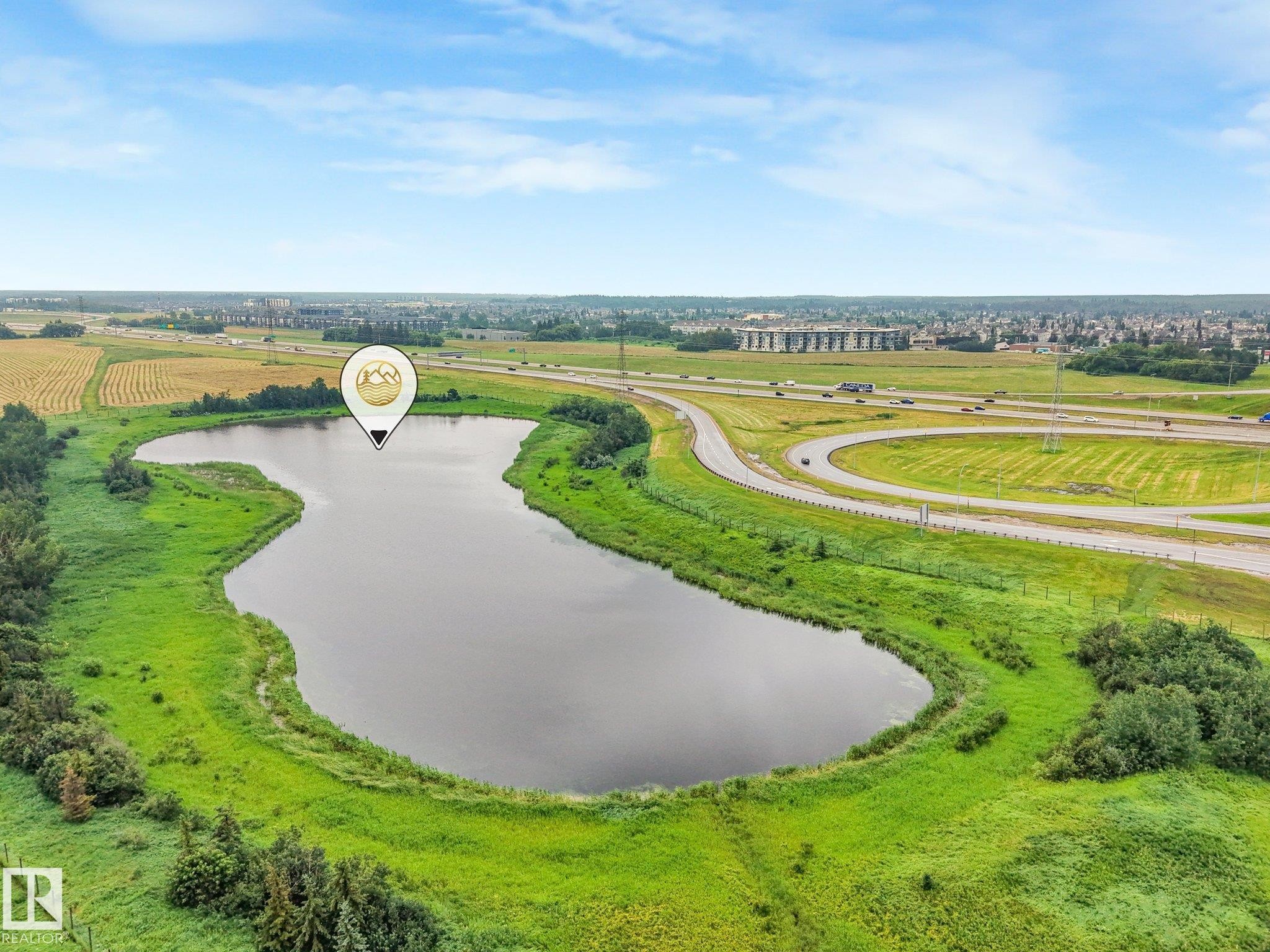 Natural body of water surrounded by green foliage, with highways and distant structures visible under a clear sky - 18611 57 Avenue Nw, Edmonton, AB - Outdoor With View