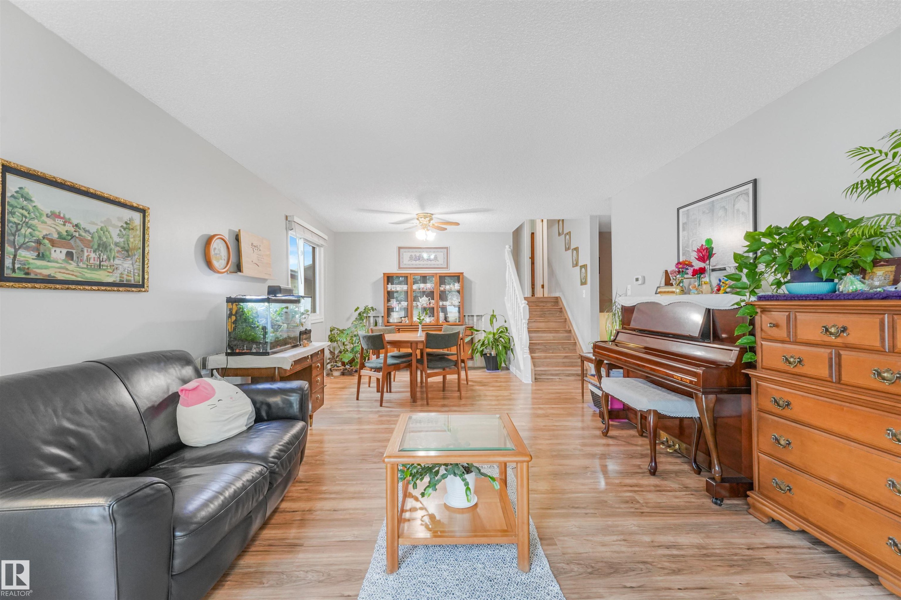 Open-concept living area featuring wood-finish flooring throughout, bright white walls, a ceiling fan, and a visible staircase - 18611 57 Avenue Nw, Edmonton, AB - Indoor Photo Showing Living Room