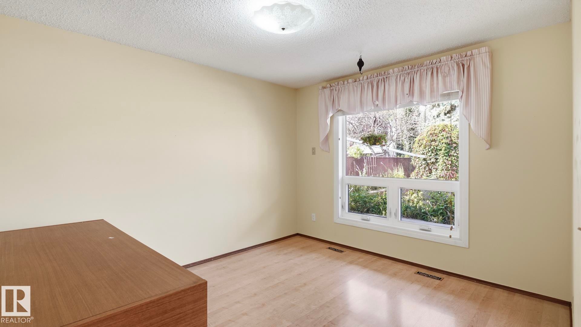 Hardwood-style flooring, neutral wall paint, and a large window with white trim - 8408 176 Street Nw, Edmonton, AB - Indoor Photo Showing Other Room