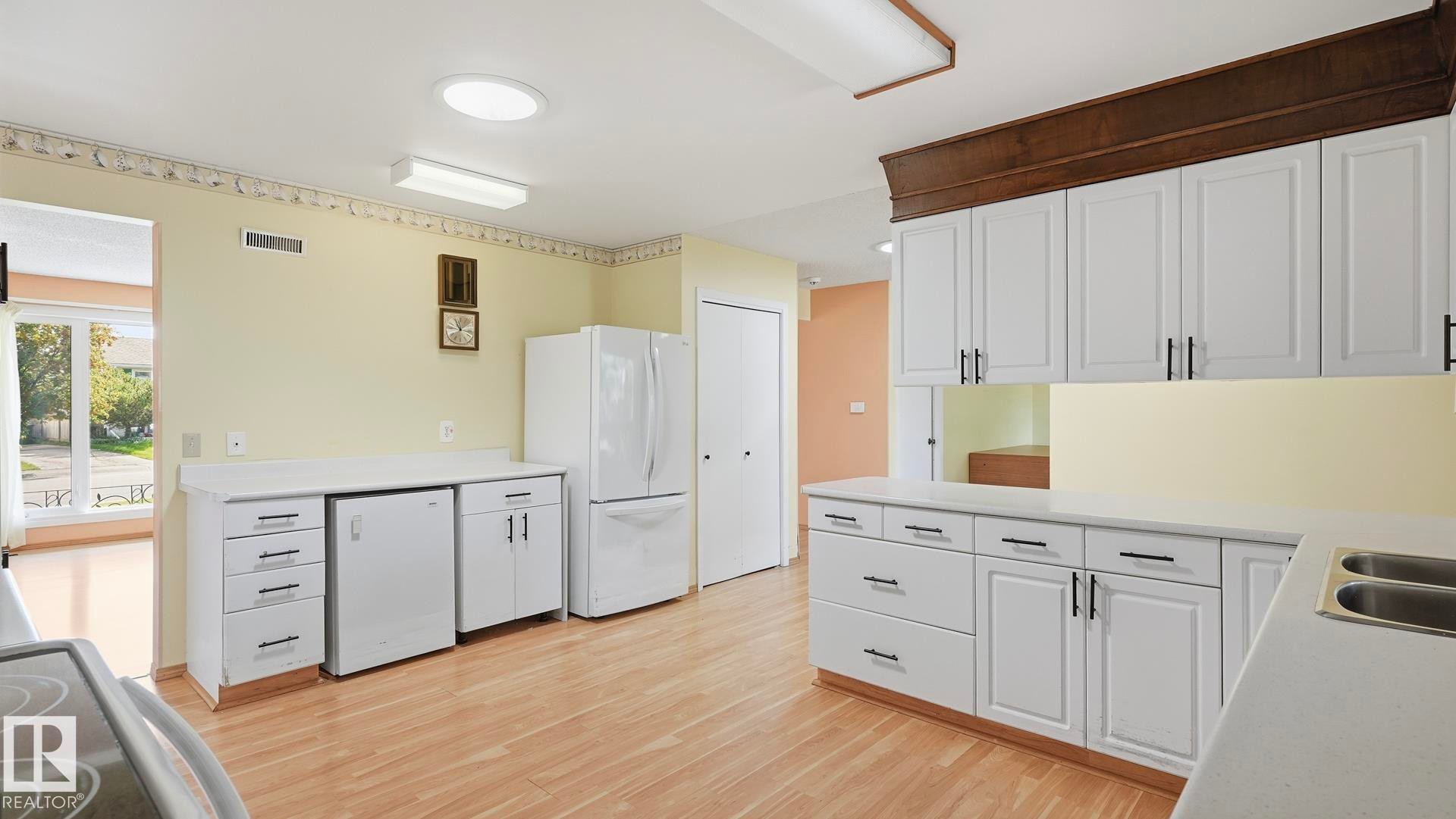 Kitchen featuring white cabinetry, light countertops, wood-finish flooring, and white appliances - 8408 176 Street Nw, Edmonton, AB - Indoor Photo Showing Kitchen With Double Sink