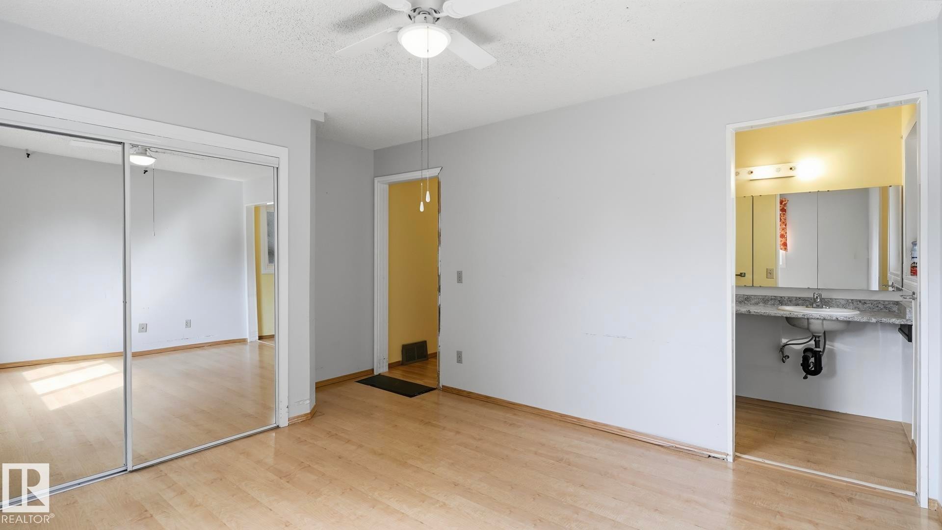 Wood-finish flooring, mirrored closet doors, ceiling fan with integrated lighting, and a bathroom with a vanity and sink - 8408 176 Street Nw, Edmonton, AB - Indoor Photo Showing Other Room