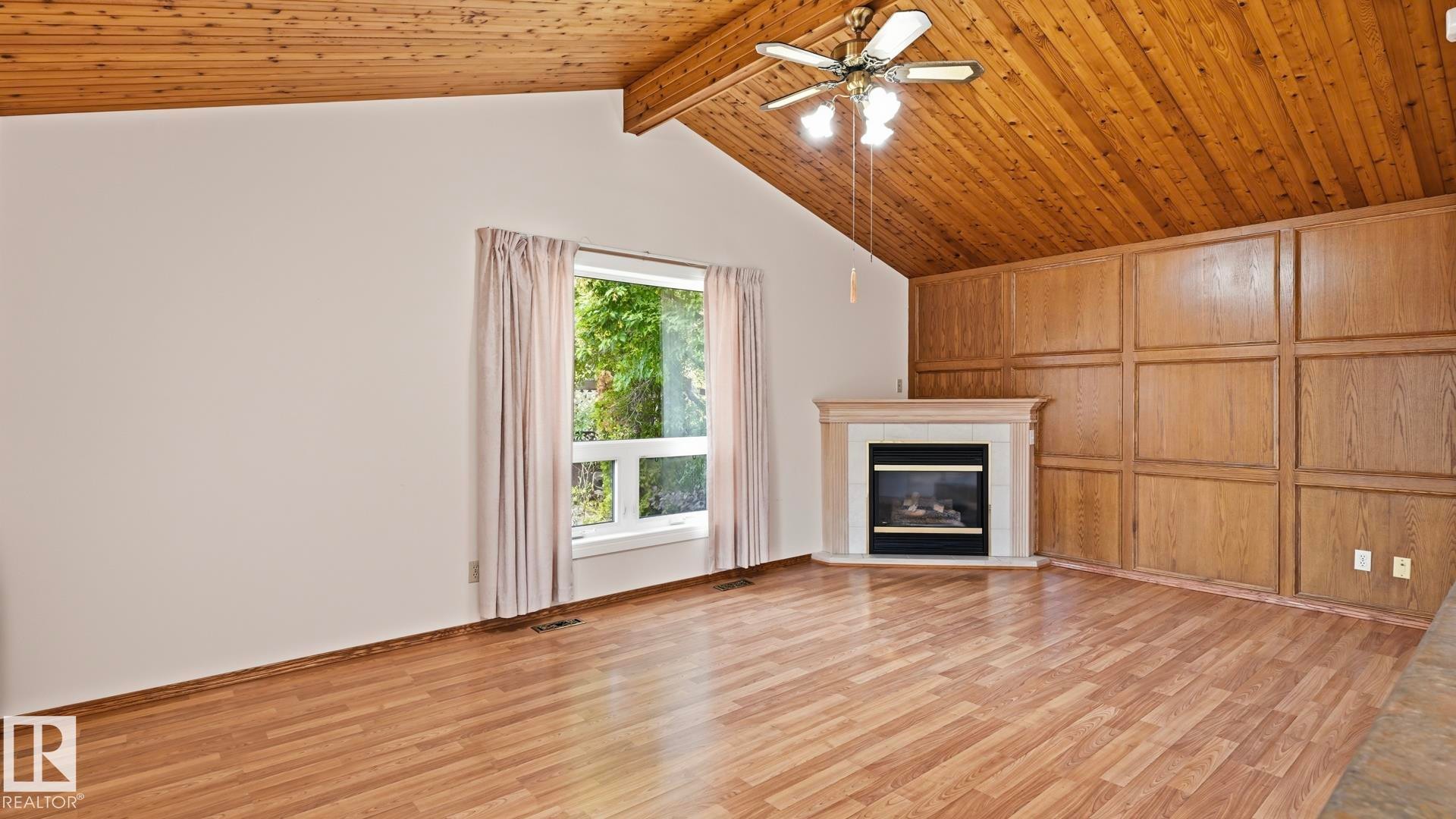Vaulted wood-paneled ceiling, wood-finish flooring, corner fireplace with a mantel, wood-paneled accent wall, and a ceiling fan with integrated lighting - 8408 176 Street Nw, Edmonton, AB - Indoor Photo Showing Living Room With Fireplace