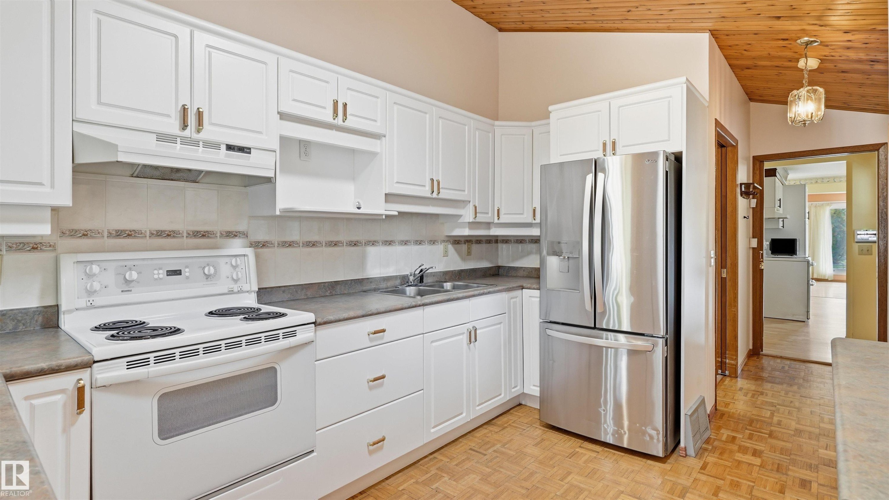 White cabinetry with gold-tone hardware, stainless steel refrigerator, white electric range with range hood, wood-finish flooring, and a wood-paneled ceiling - 8408 176 Street Nw, Edmonton, AB - Indoor Photo Showing Kitchen
