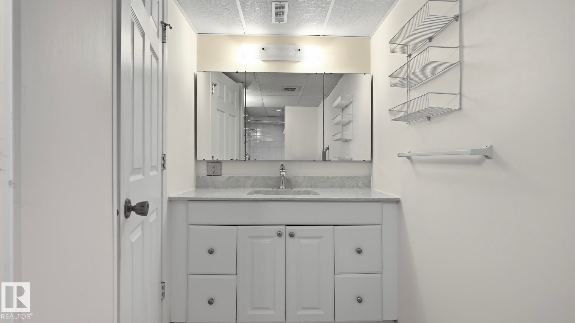 White vanity with integrated sink, chrome faucet, wall-mounted mirror, and overhead lighting - 8408 176 Street Nw, Edmonton, AB - Indoor Photo Showing Bathroom