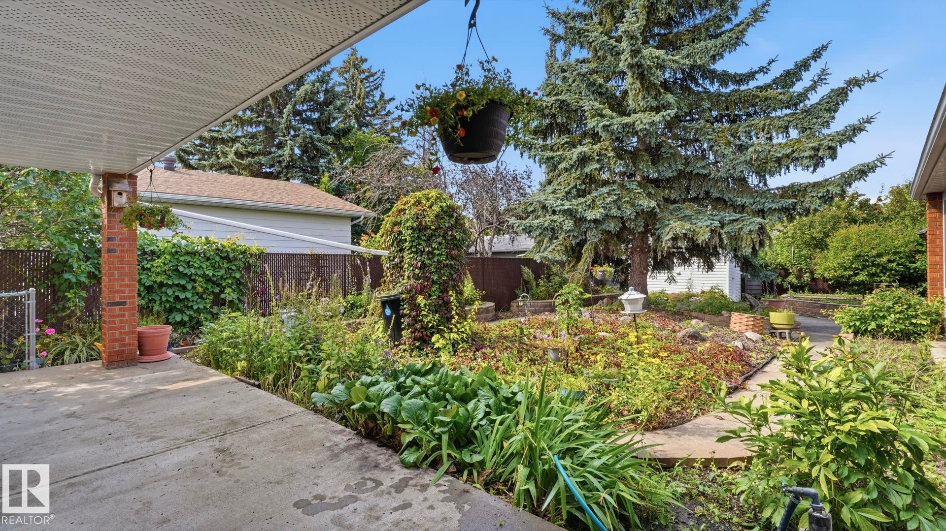 Carport with a brick column, concrete patio, established garden beds, mature trees, and a storage shed - 8408 176 Street Nw, Edmonton, AB - Outdoor