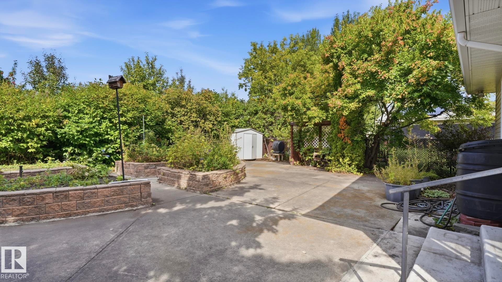 Concrete patio with raised garden beds featuring stacked stone retaining walls - 8408 176 Street Nw, Edmonton, AB - Outdoor