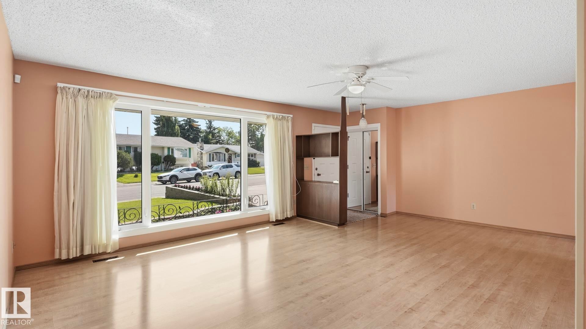 Expansive room featuring wood-finish flooring, a large picture window, a built-in wood-toned room divider, and a ceiling fan with integrated lighting - 8408 176 Street Nw, Edmonton, AB - Indoor Photo Showing Other Room