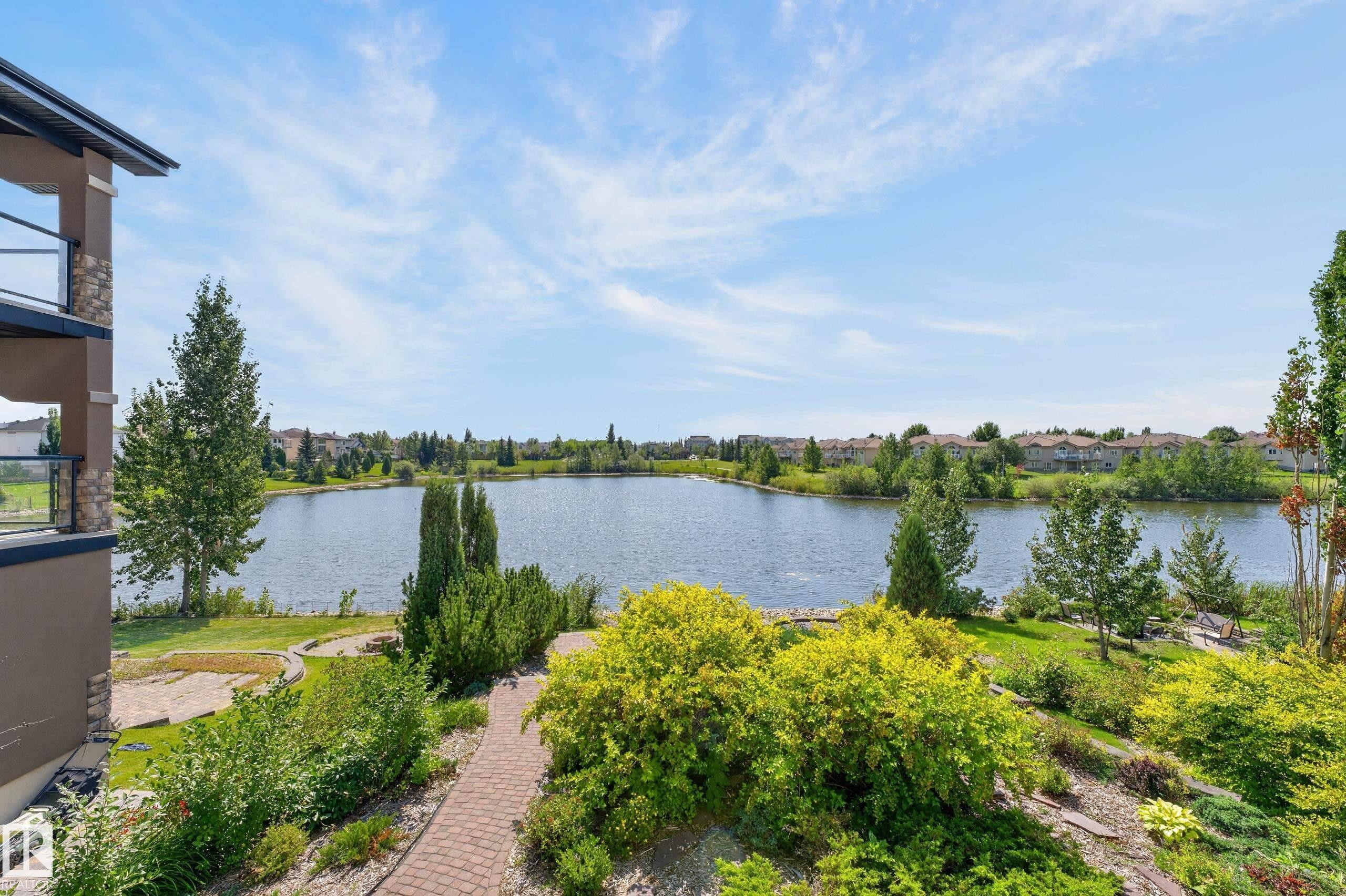 Expansive lakefront setting with lush landscaping, a winding brick paver pathway, and a multi-level balcony featuring glass railings - 13527 158 Avenue Nw, Edmonton, AB - Outdoor With Body Of Water With View