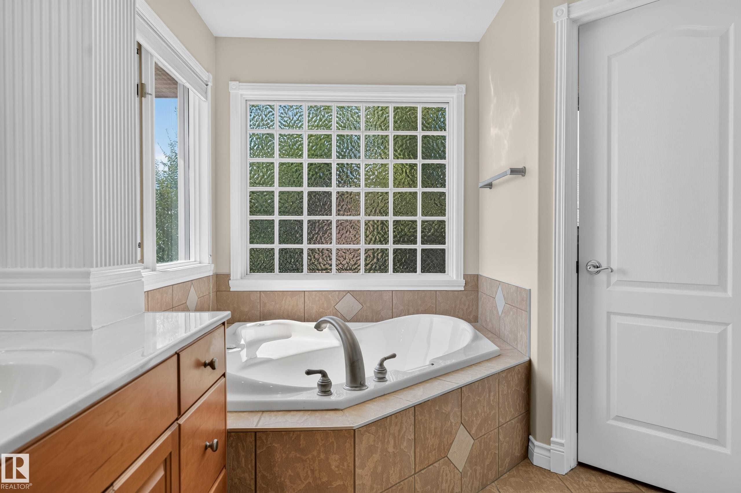 Built-in soaking tub with brushed nickel fixtures, complemented by a glass block window and a tiled surround - 13527 158 Avenue Nw, Edmonton, AB - Indoor Photo Showing Bathroom