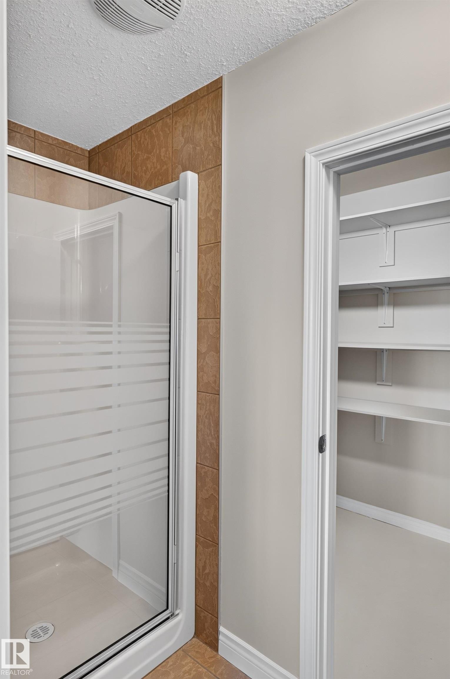 Walk-in shower with frosted glass enclosure, tile surround, and an adjacent built-in closet with shelving - 13527 158 Avenue Nw, Edmonton, AB - Indoor