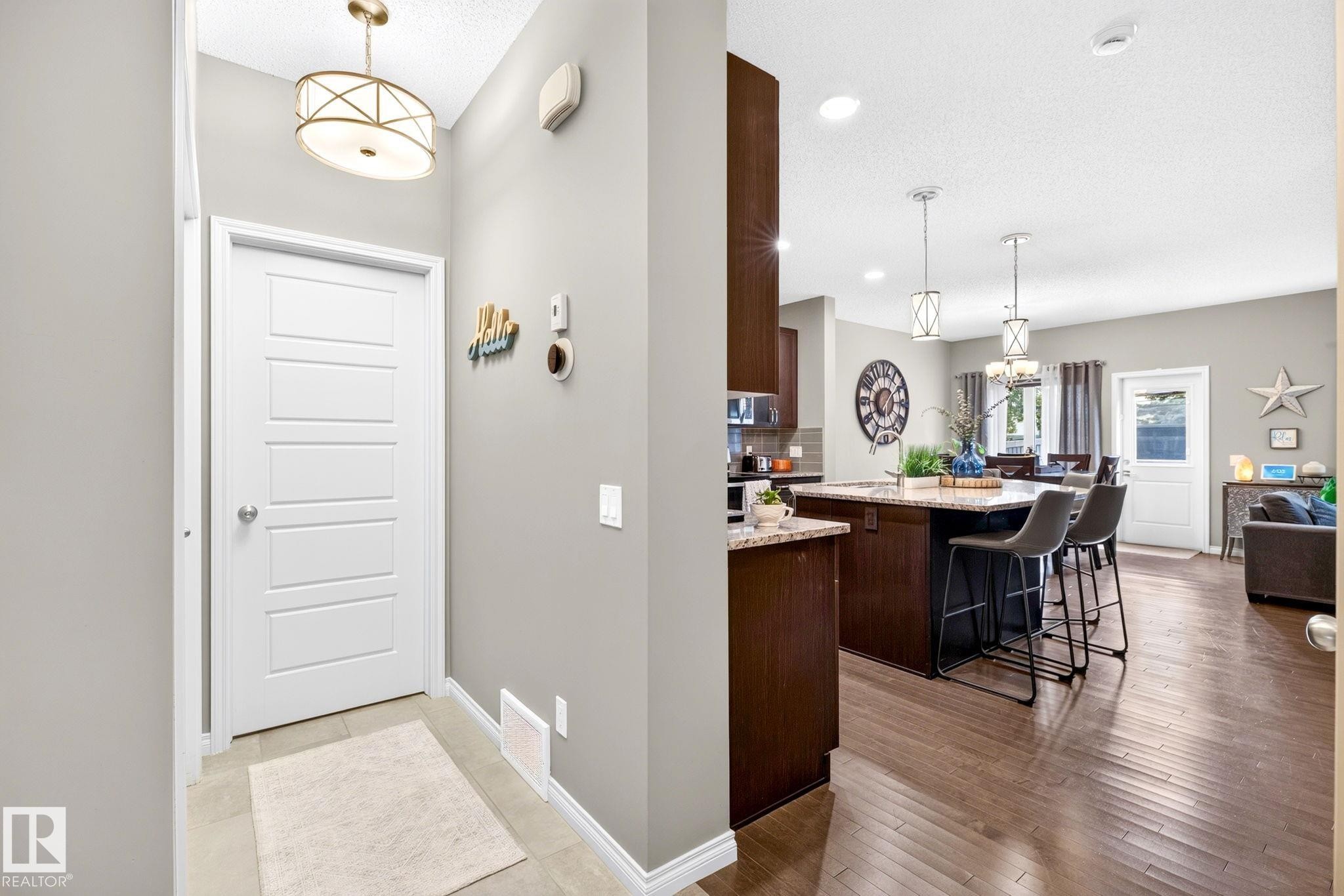 Open-concept living space with dark wood-finish flooring, a kitchen island with seating, a dining area, and a white paneled door - 16512 140 Street Nw, Edmonton, AB - Indoor