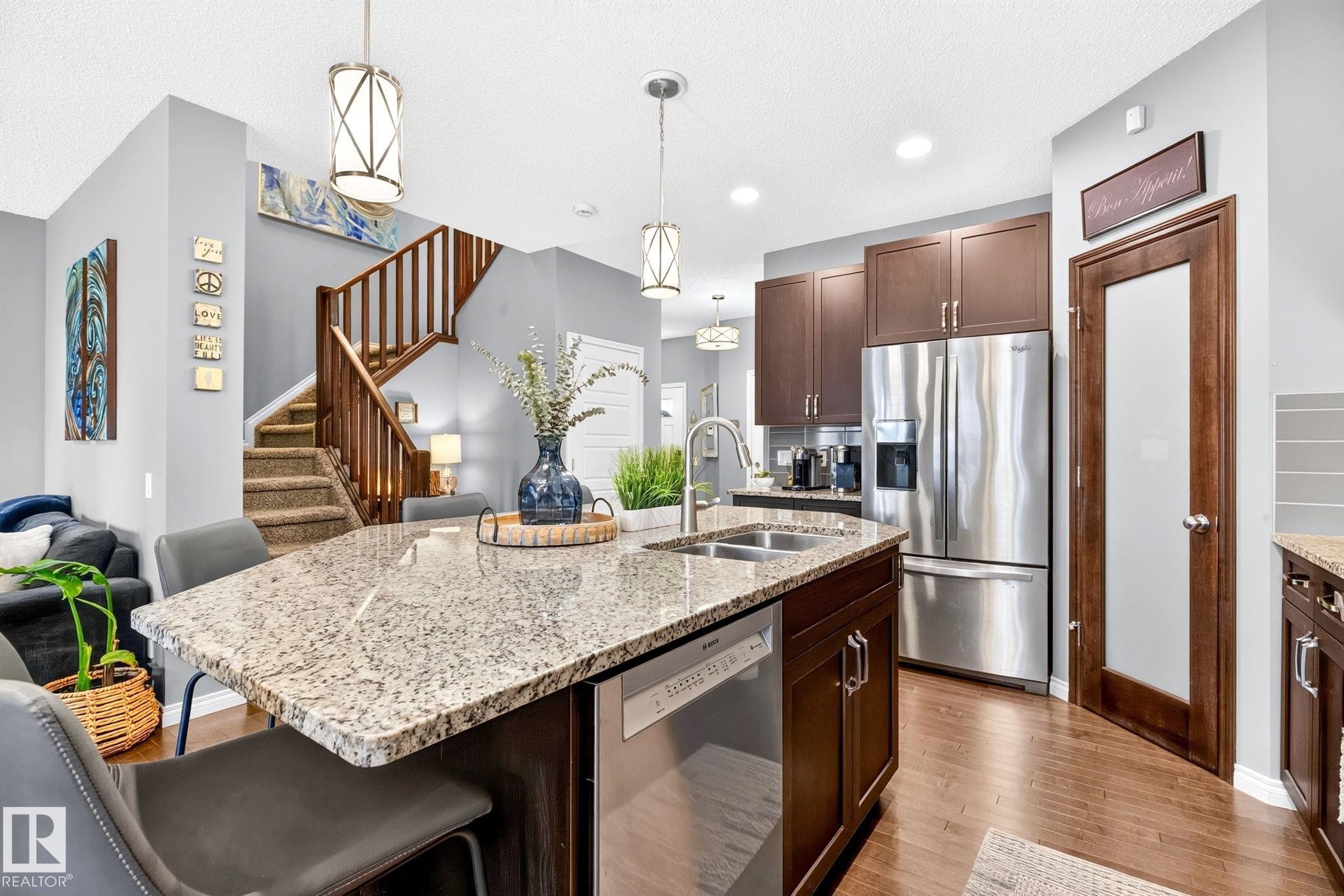 Kitchen island with an undermount double basin sink, stainless steel dishwasher, and seating for three - 16512 140 Street Nw, Edmonton, AB - Indoor Photo Showing Kitchen With Double Sink With Upgraded Kitchen