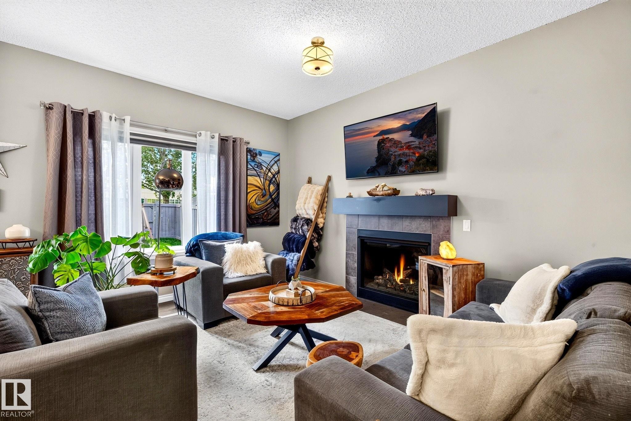 Tile-surround fireplace with a dark mantel, large window, and overhead lighting - 16512 140 Street Nw, Edmonton, AB - Indoor Photo Showing Living Room With Fireplace