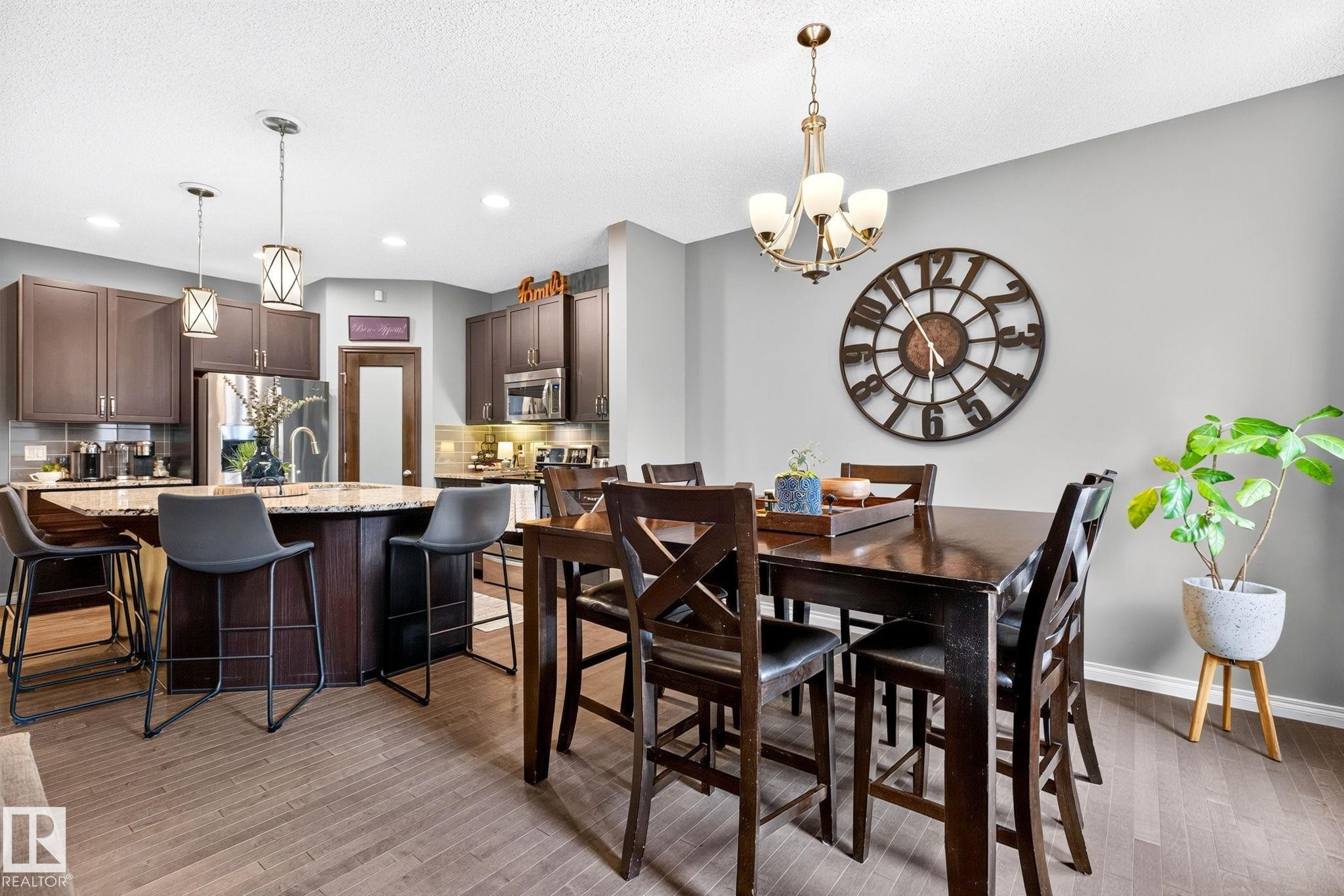Open-concept living space with wood-finish flooring, a kitchen island featuring a light-toned countertop, and dark wood cabinetry - 16512 140 Street Nw, Edmonton, AB - Indoor Photo Showing Dining Room