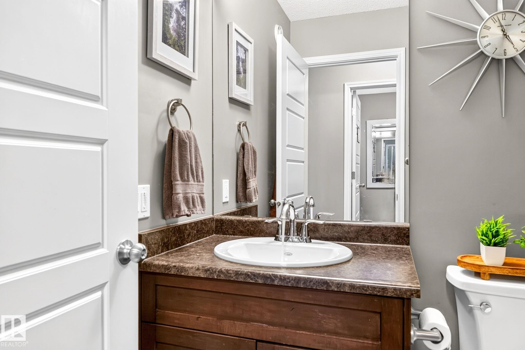 Powder room featuring a wood-finish vanity with an integrated sink, polished chrome faucet, and full-width mirror - 16512 140 Street Nw, Edmonton, AB - Indoor Photo Showing Bathroom