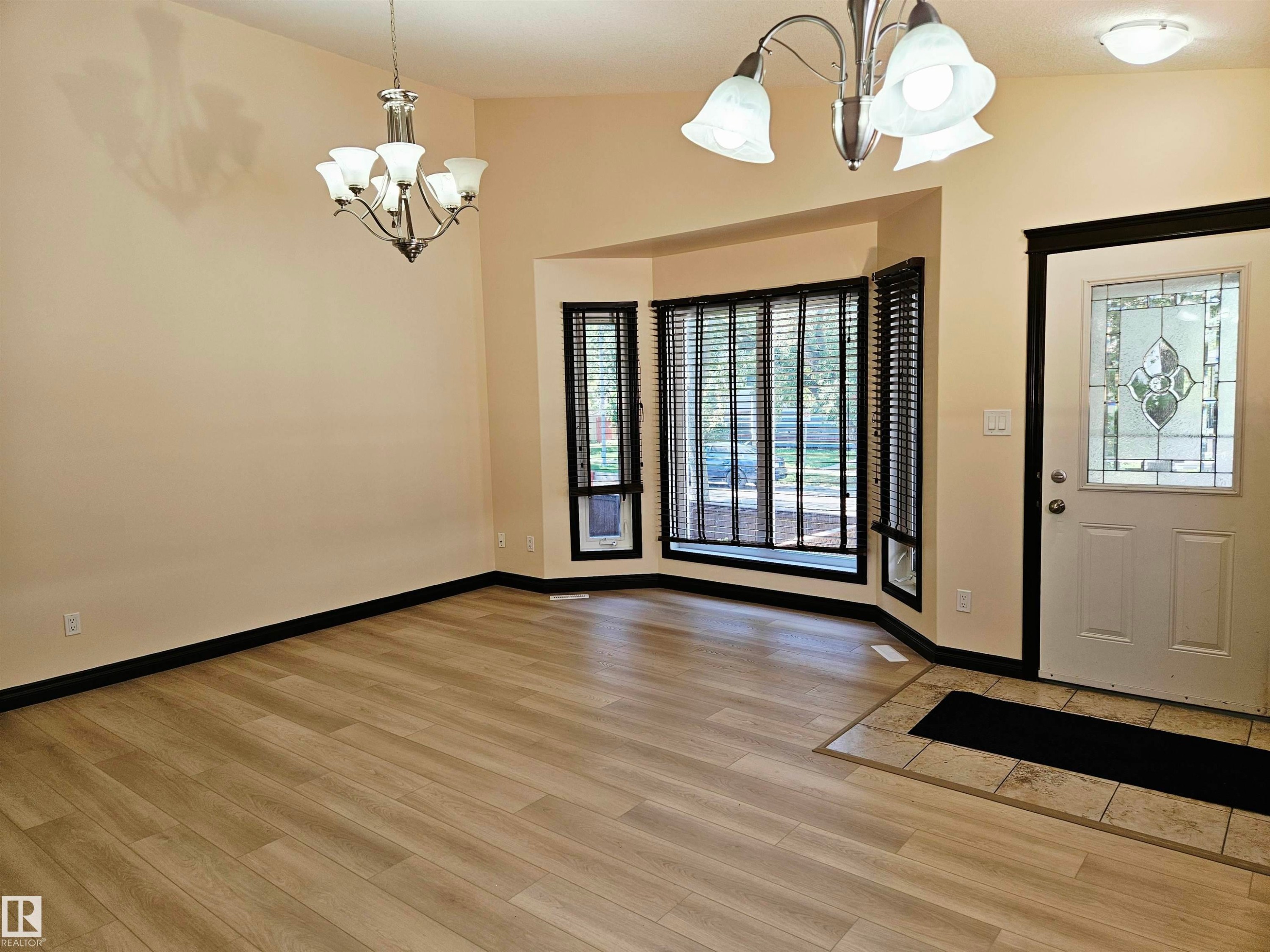 Wood-finish flooring, bay window with blinds, decorative front entry door, and two chandelier light fixtures - 11625 88 Street Nw, Edmonton, AB